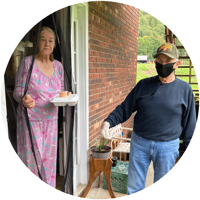 A man wearing a mask is standing next to a woman holding a tray.