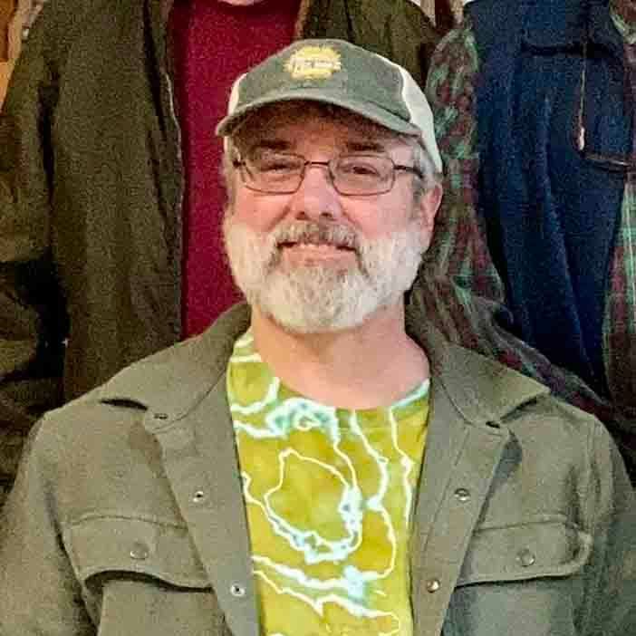 A man with a beard and glasses is wearing a hat and a green jacket.