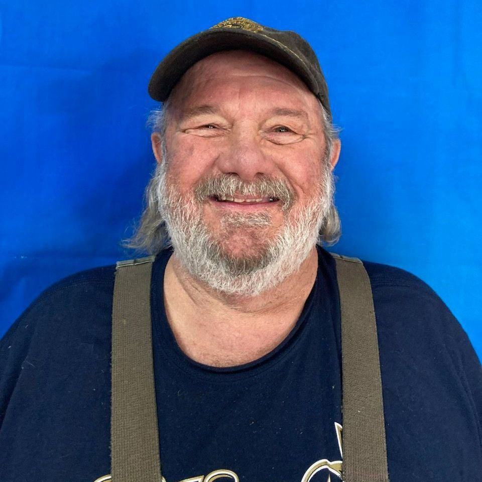 A man with a beard and suspenders is smiling for the camera