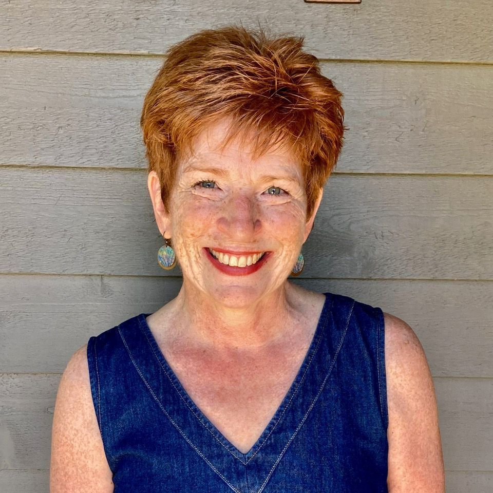 A woman wearing a blue tank top and earrings smiles for the camera