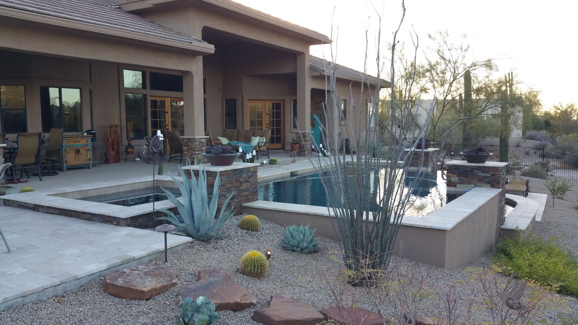 Backyard patio with a swimming pool, desert plants, and a covered outdoor seating area at sunset