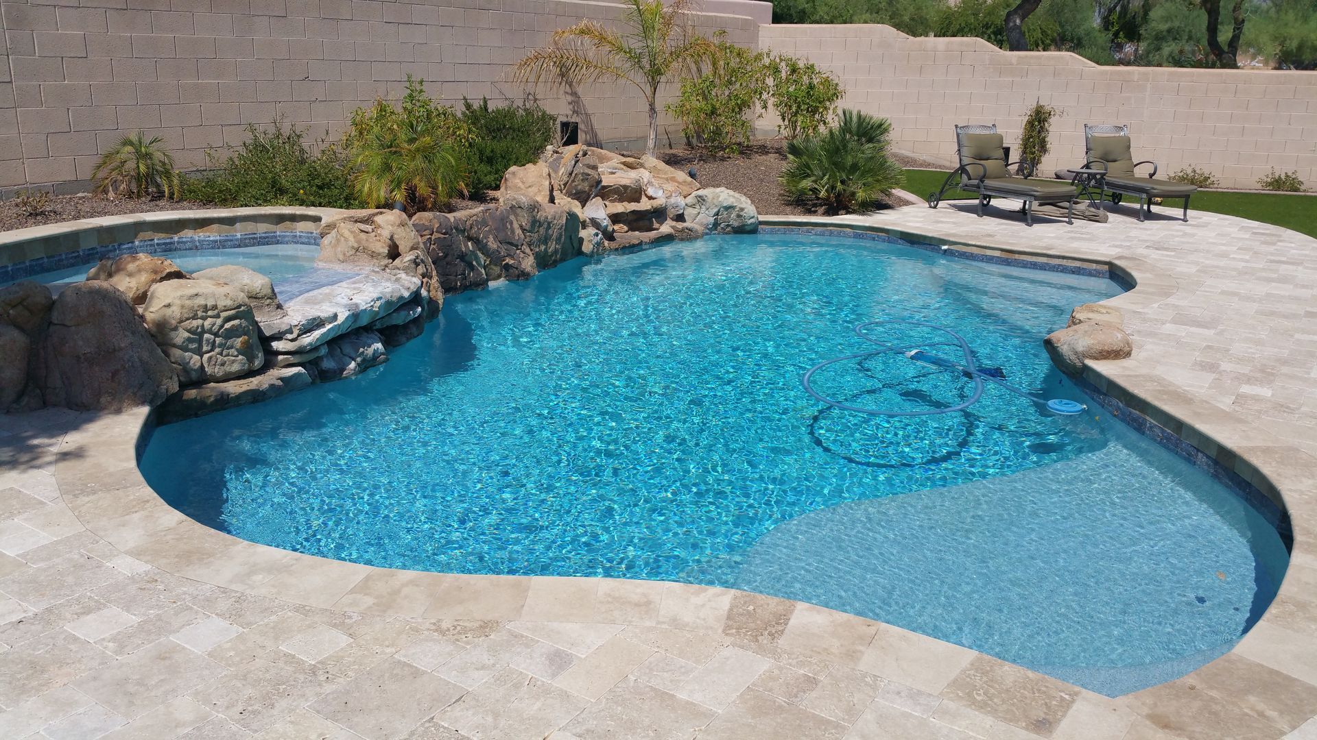 Backyard swimming pool with blue water, stone deck, and rock waterfall feature