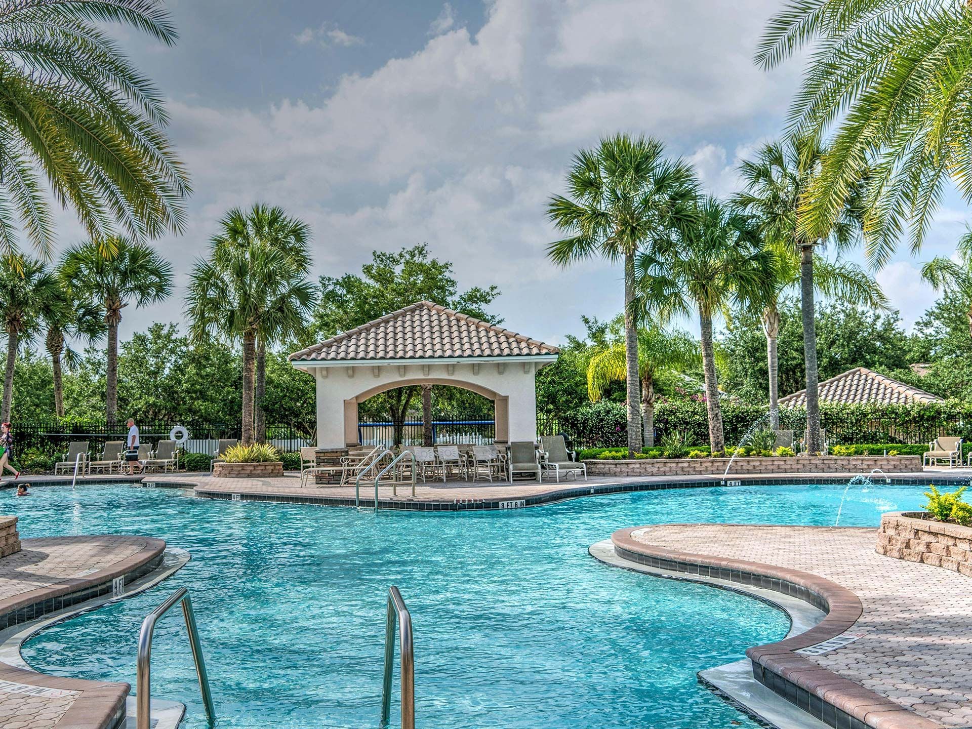 Tropical resort pool with turquoise water, palm trees, and a white gazebo under a cloudy sky