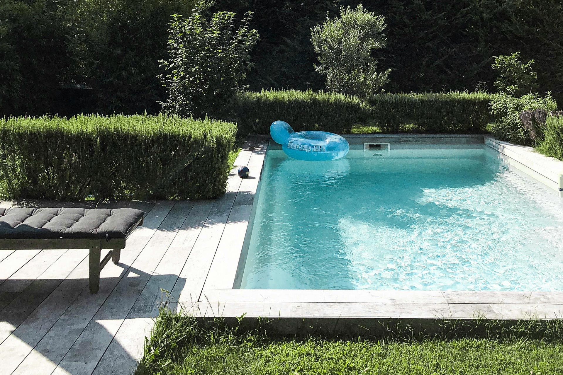 Backyard swimming pool with turquoise water, white deck, lounge chair, and green hedges in sunlight