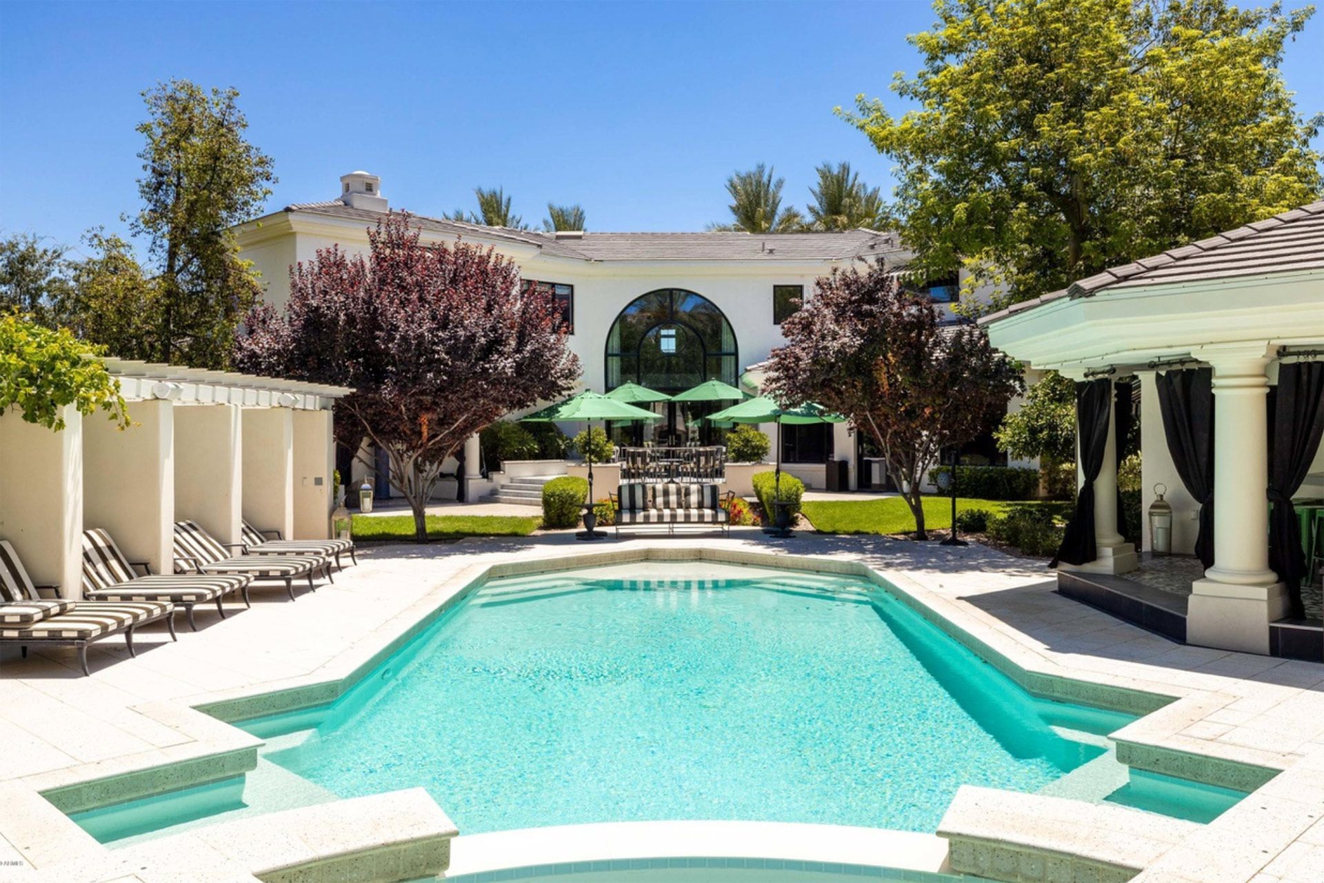 Luxury backyard with turquoise pool, white lounge chairs, and a modern house under sunny trees