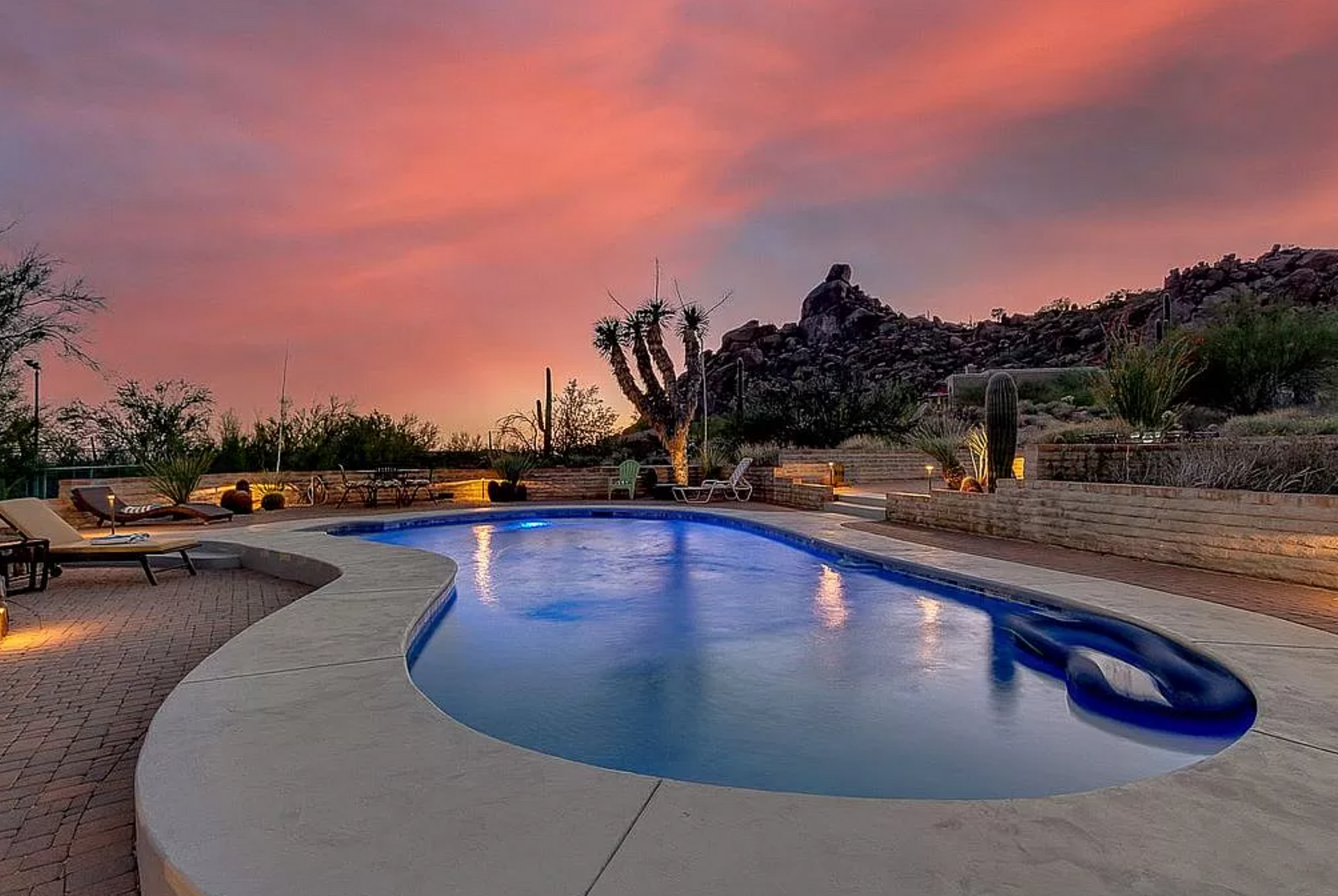 Backyard pool at sunset with blue water, desert landscaping, and pink-orange sky