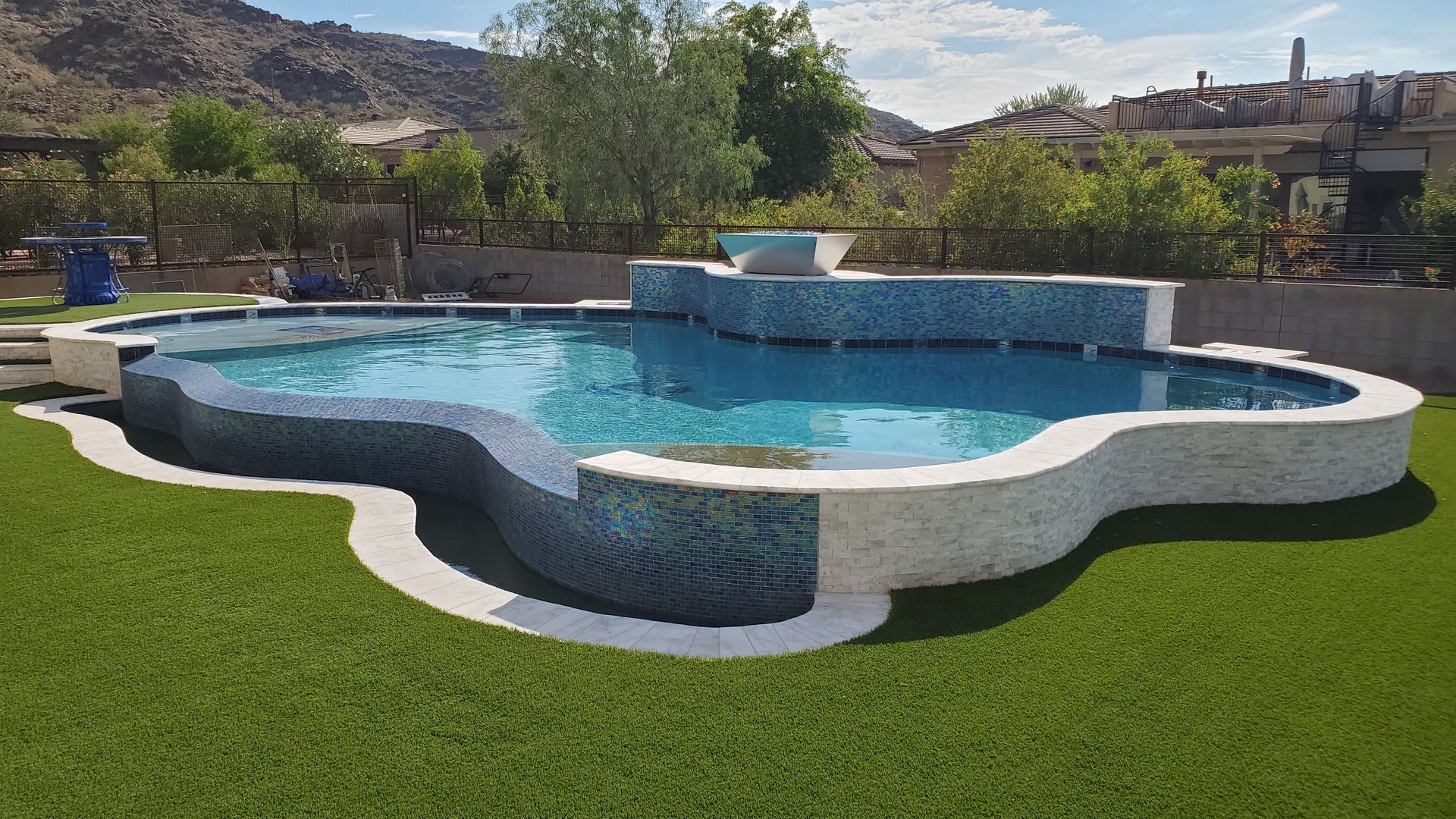Freeform blue swimming pool with white stone edging on a green lawn in a sunny outdoor resort setting