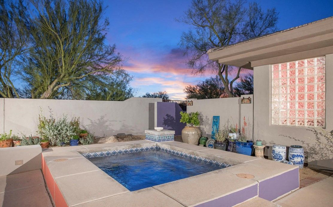 Backyard pool patio at sunset with blue water, white walls, and outdoor seating