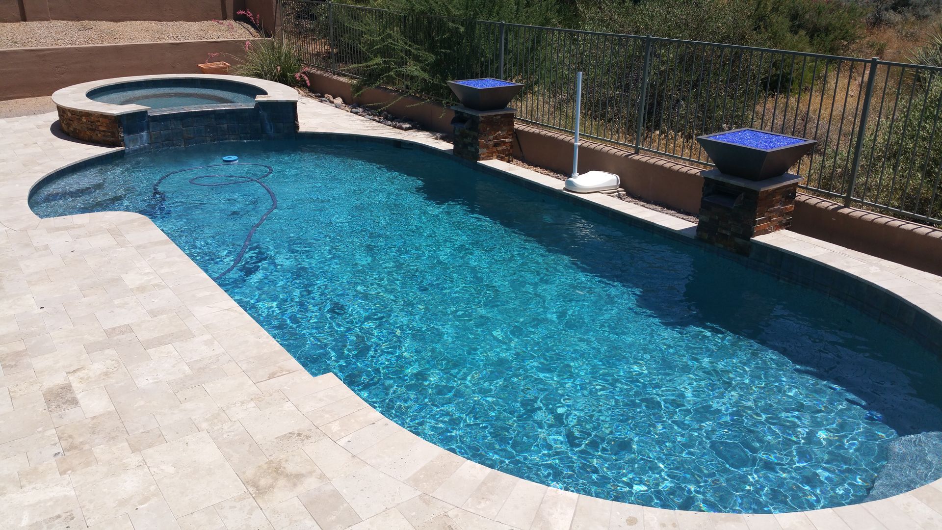 Backyard swimming pool with blue water, stone deck, and raised spa