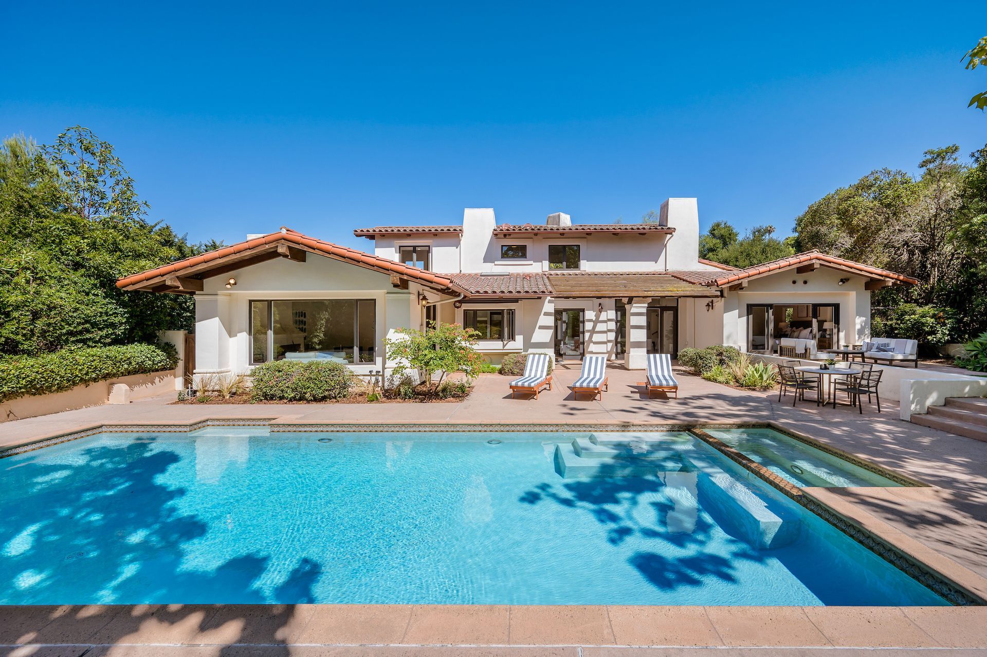 Luxury villa with a blue swimming pool, lounge chairs, and a sunny patio under a clear sky