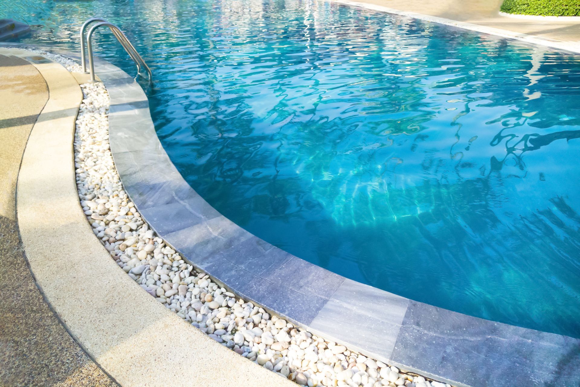Curved swimming pool edge with blue water and beige stone coping in bright sunlight