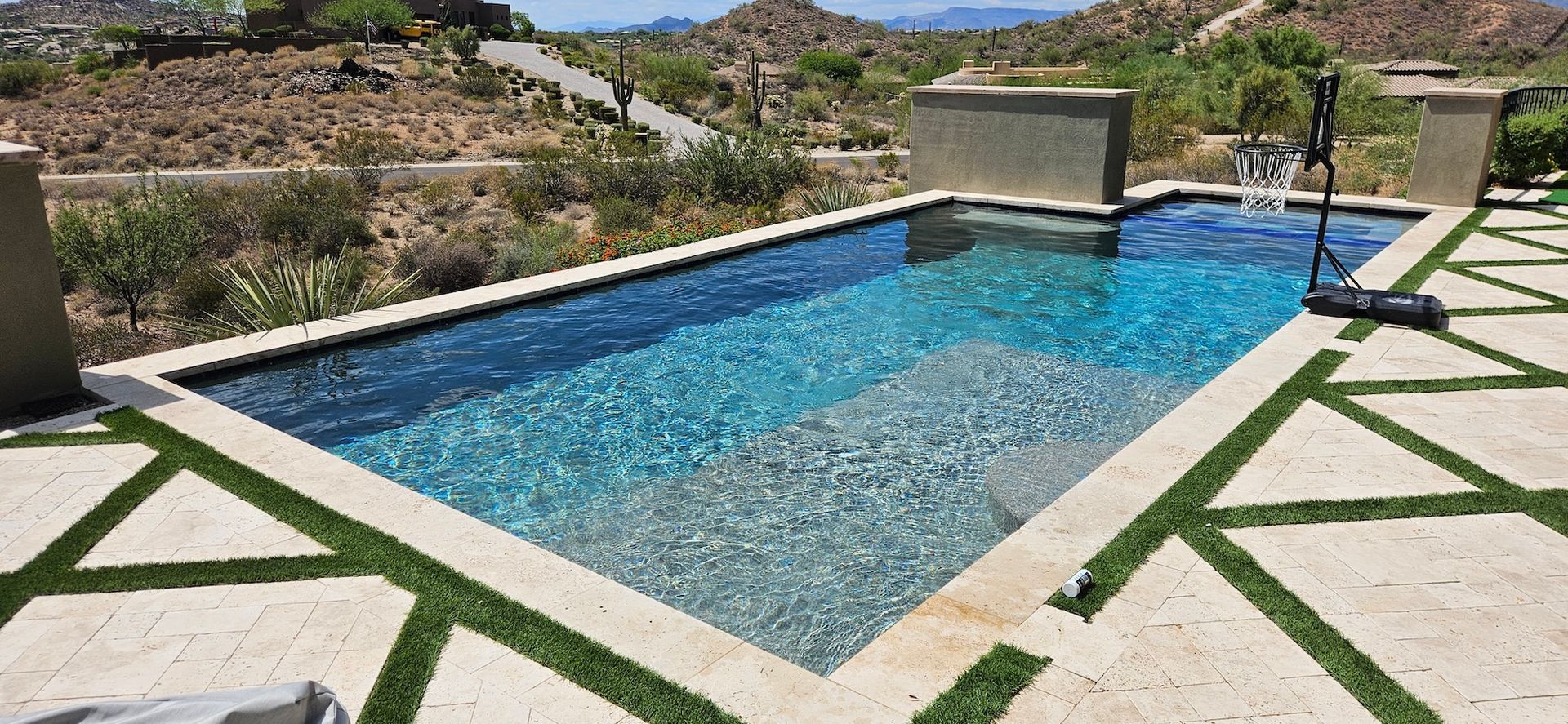 Rectangular blue pool with stone deck, set in a rocky desert landscape under a clear sky