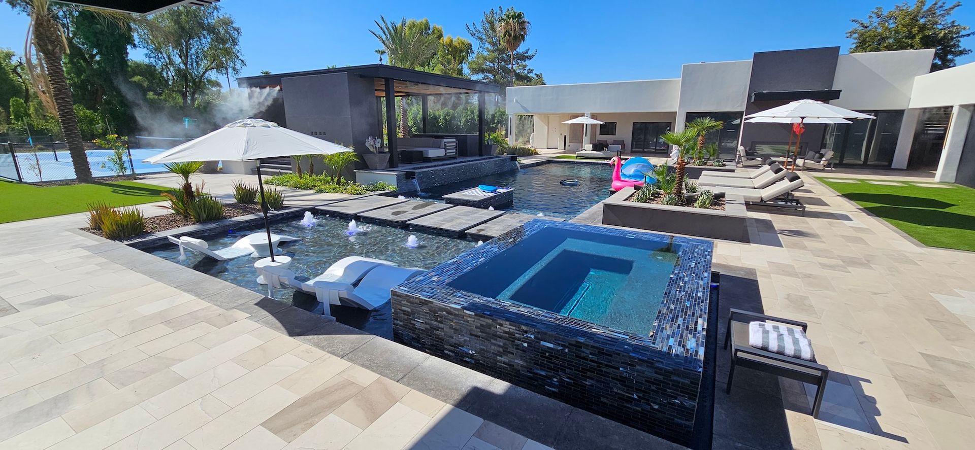 Modern backyard with a pool, patio seating, umbrellas, and lounge chairs in bright sunlight
