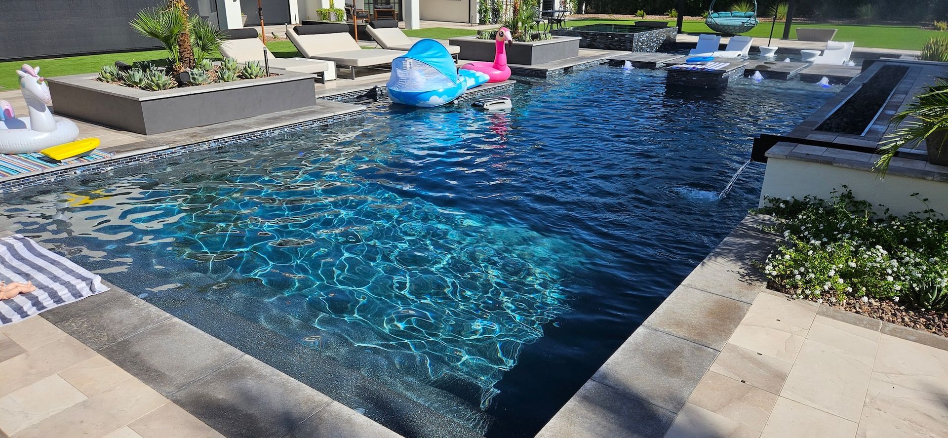 Backyard pool with blue water, lounge chairs, and colorful float toys in the sun