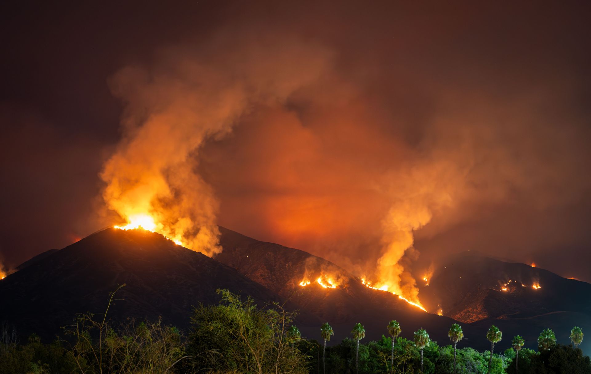 Erupción volcánica nocturna con lava de color naranja brillante y humo en una ladera oscura.