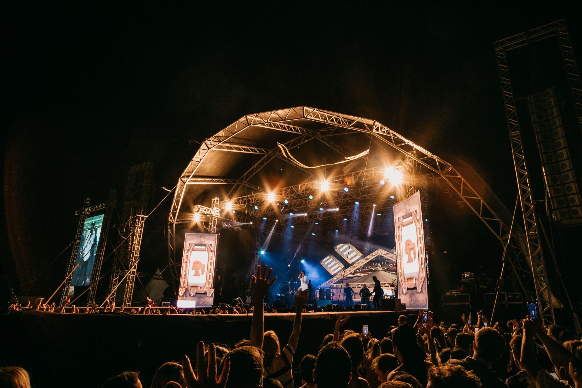 Crowded outdoor concert stage at night with bright lights and large screens
