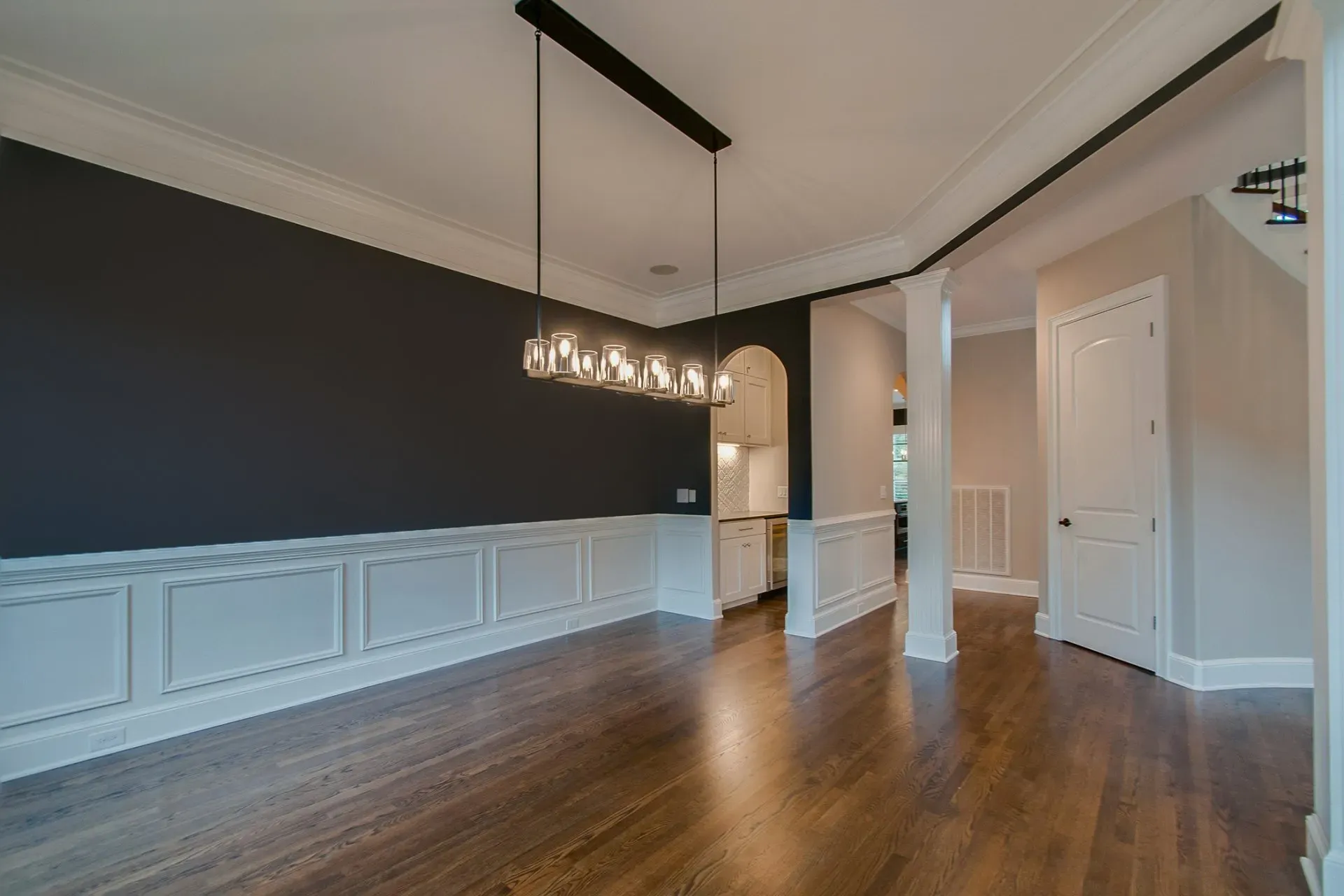 Empty dining room with dark accent wall, white wainscoting, hardwood floors, and modern pendant light