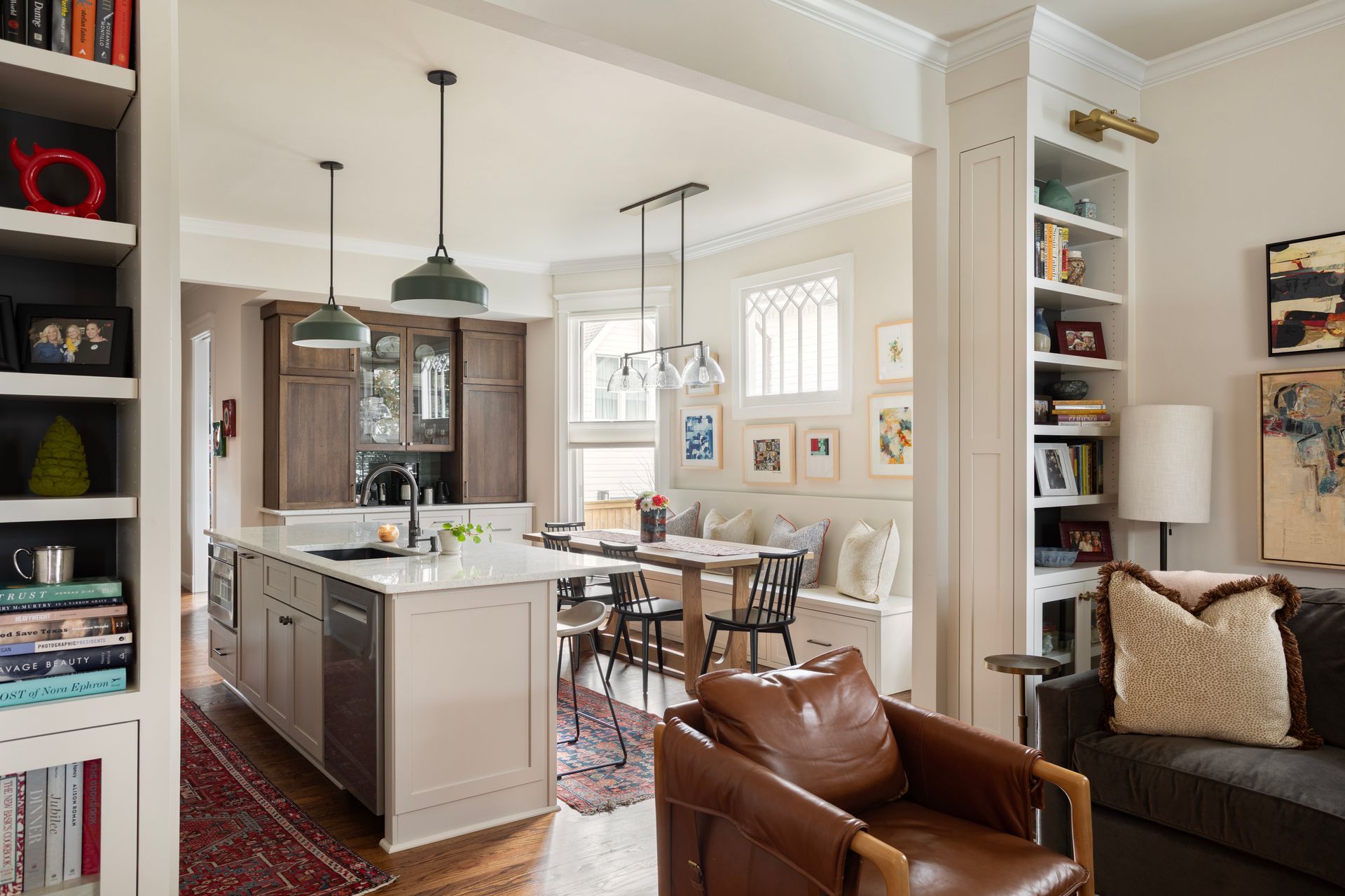 Bright open kitchen and living room with island, dining table, leather chair, and built-in shelves