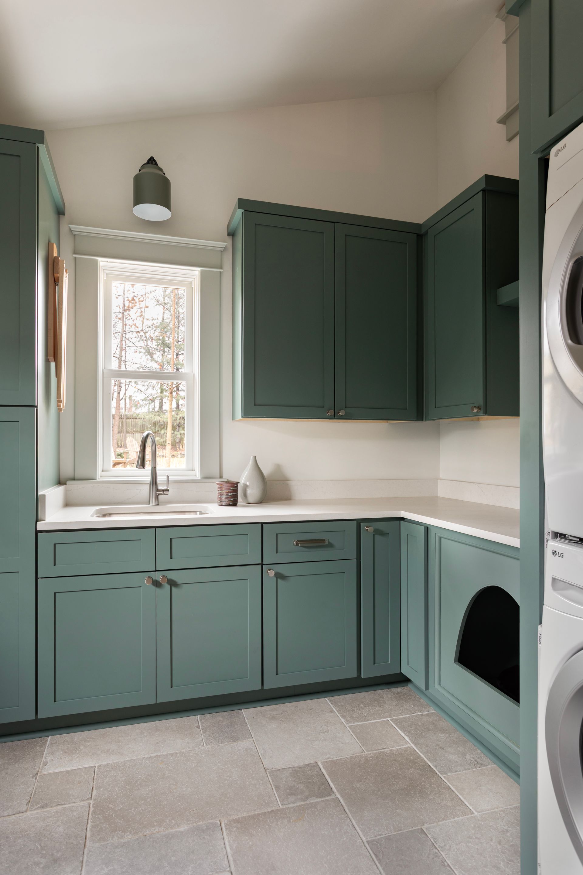 Teal kitchen with cabinets, white countertops, sink by a window, and stacked washer dryer on the right.