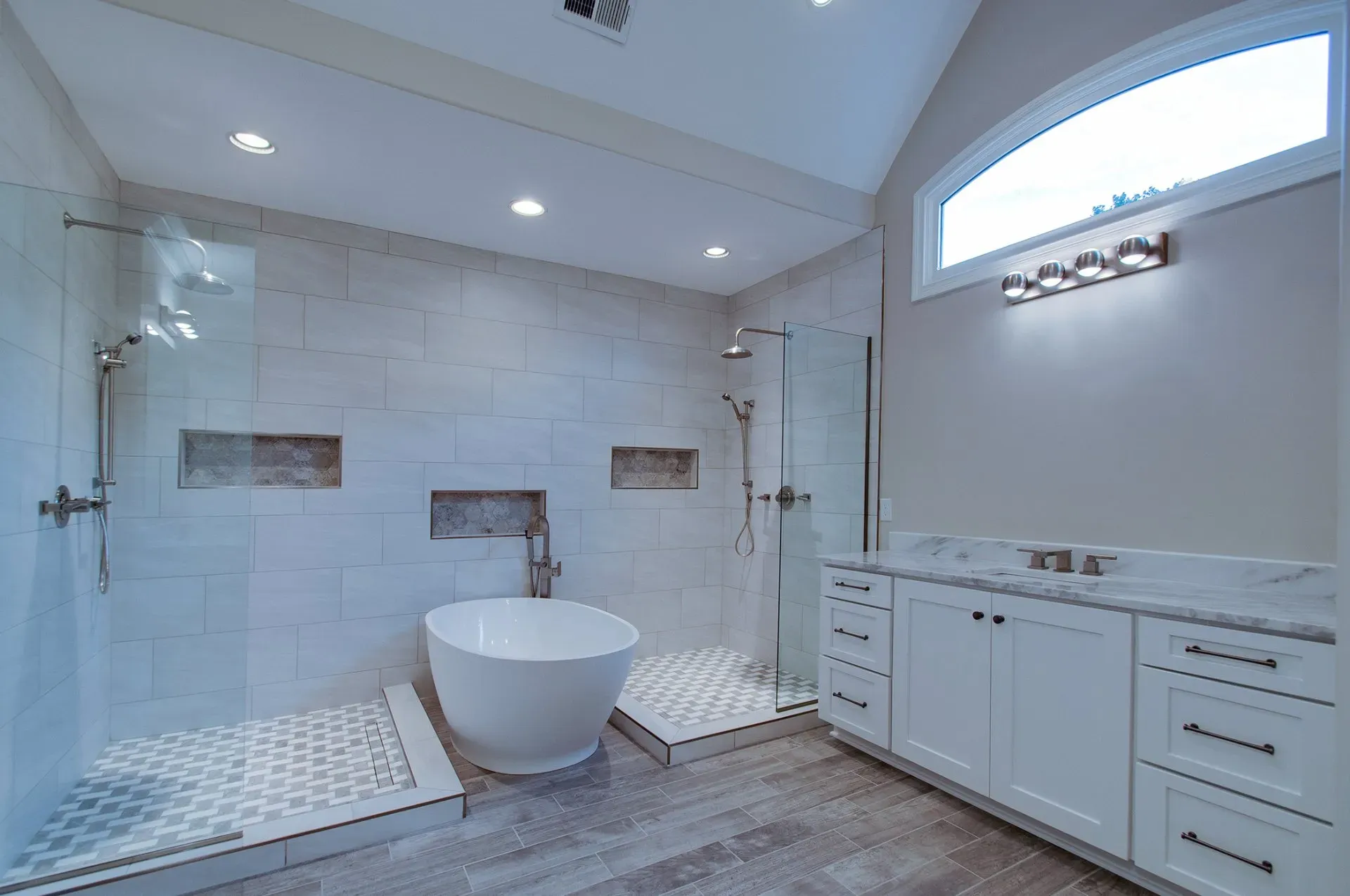 Bright modern bathroom with white tub, tiled shower, vanity, and skylight