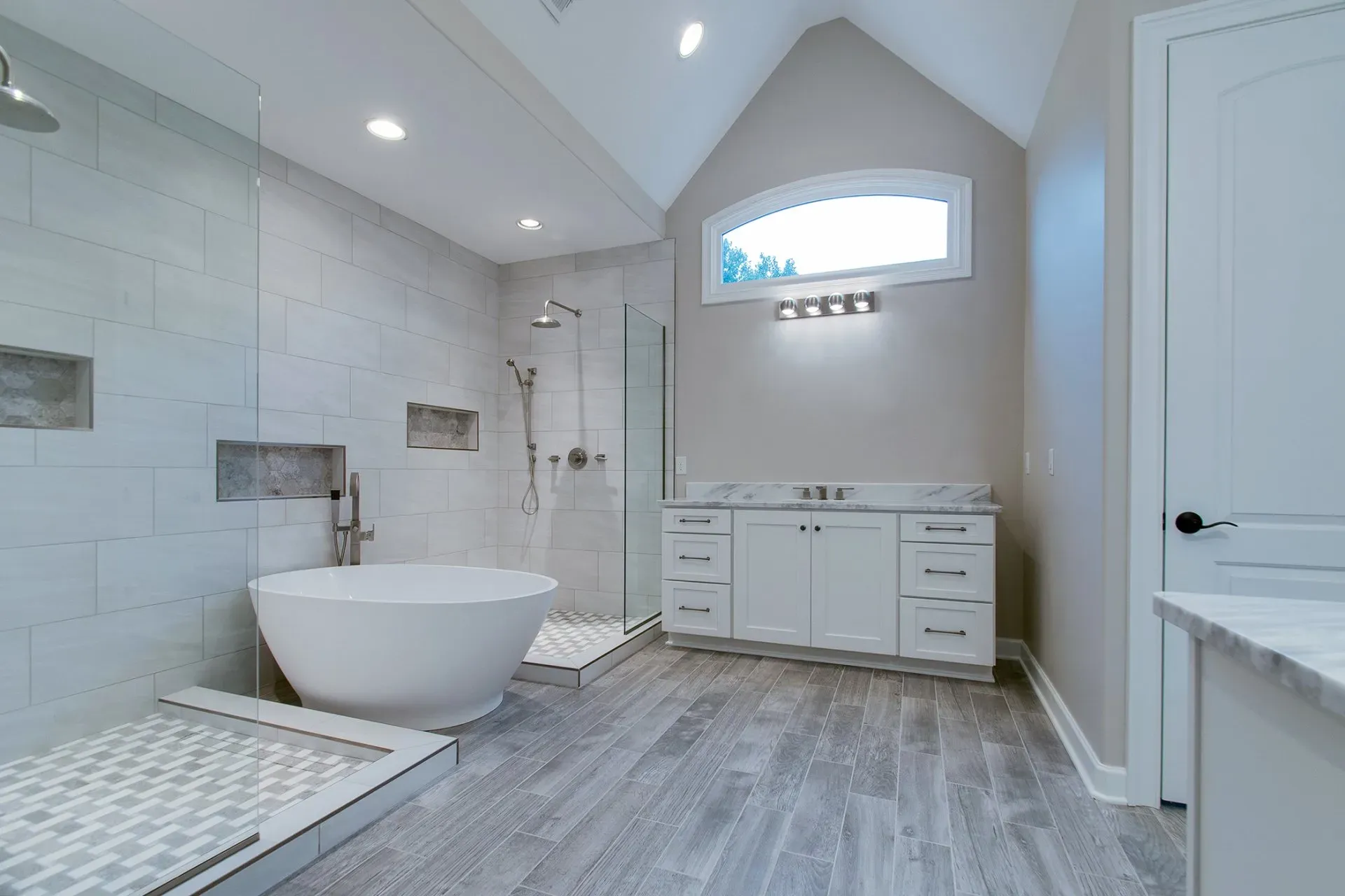 Modern white bathroom with freestanding tub, walk-in shower, double vanity, and gray wood-look flooring