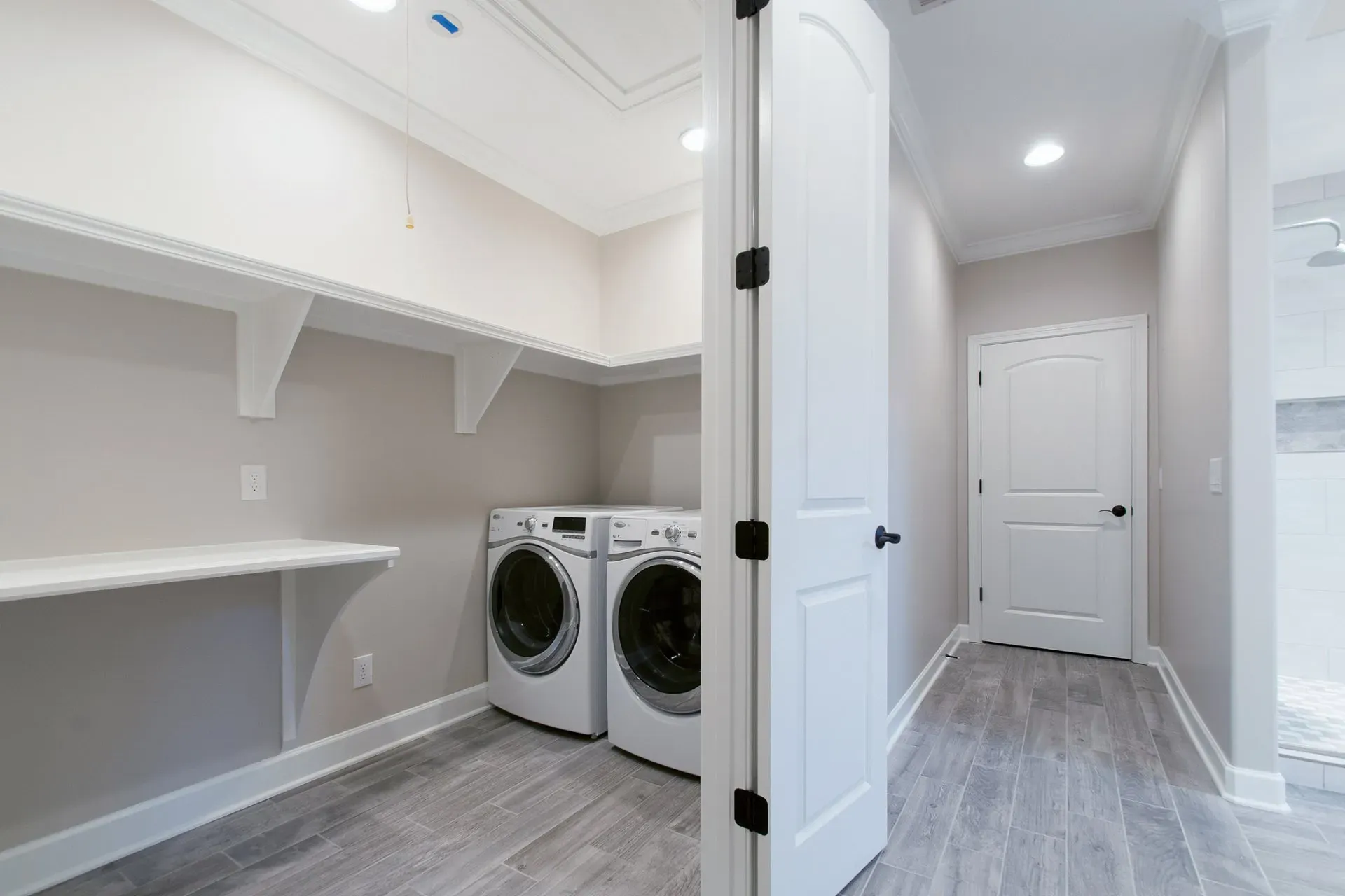 Bright laundry room with washer and dryer, white shelving, and a door leading to a hallway.