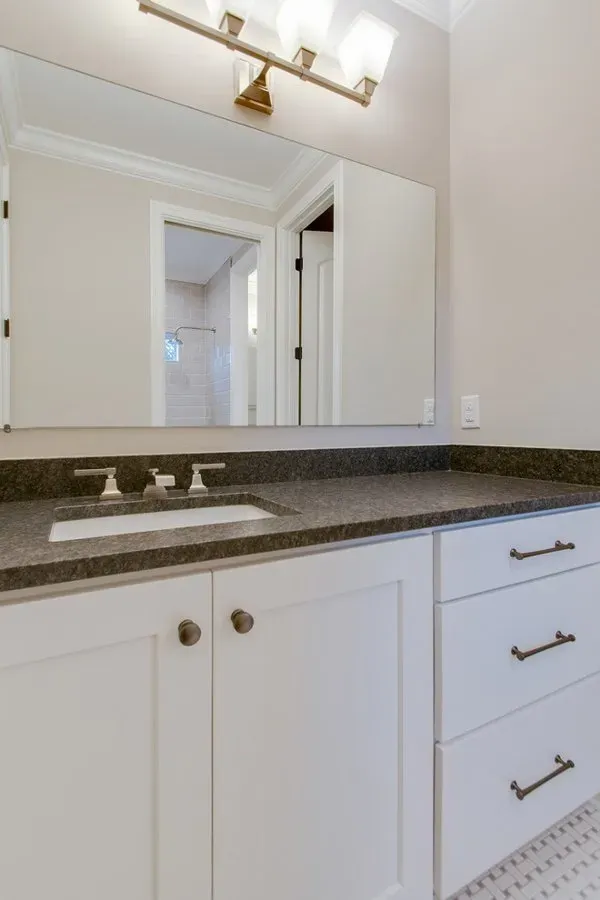 White bathroom vanity with dark countertop, sink, mirror, and gold light fixture