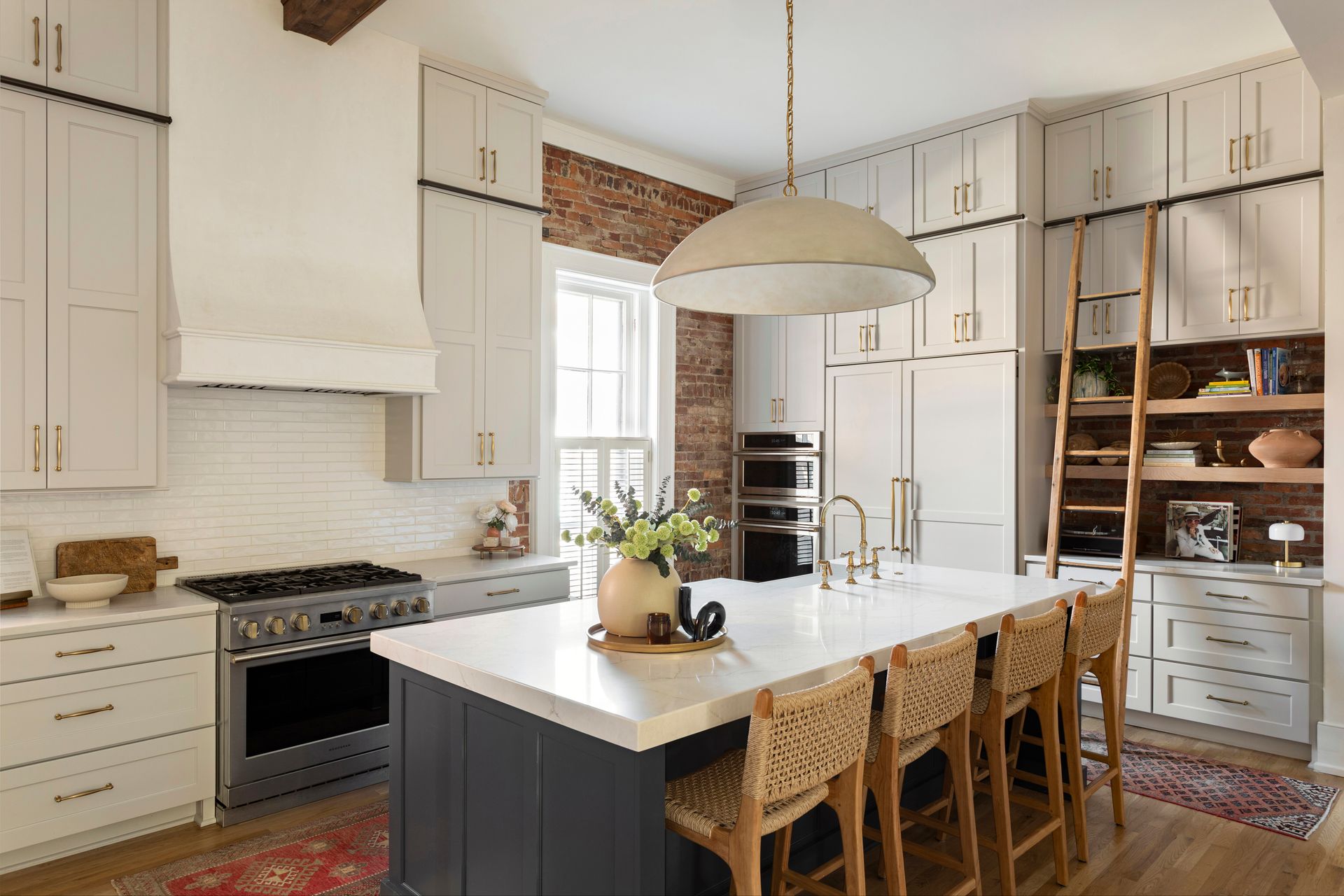Bright kitchen with white cabinets, brick accents, island, and woven barstools under a large pendant light