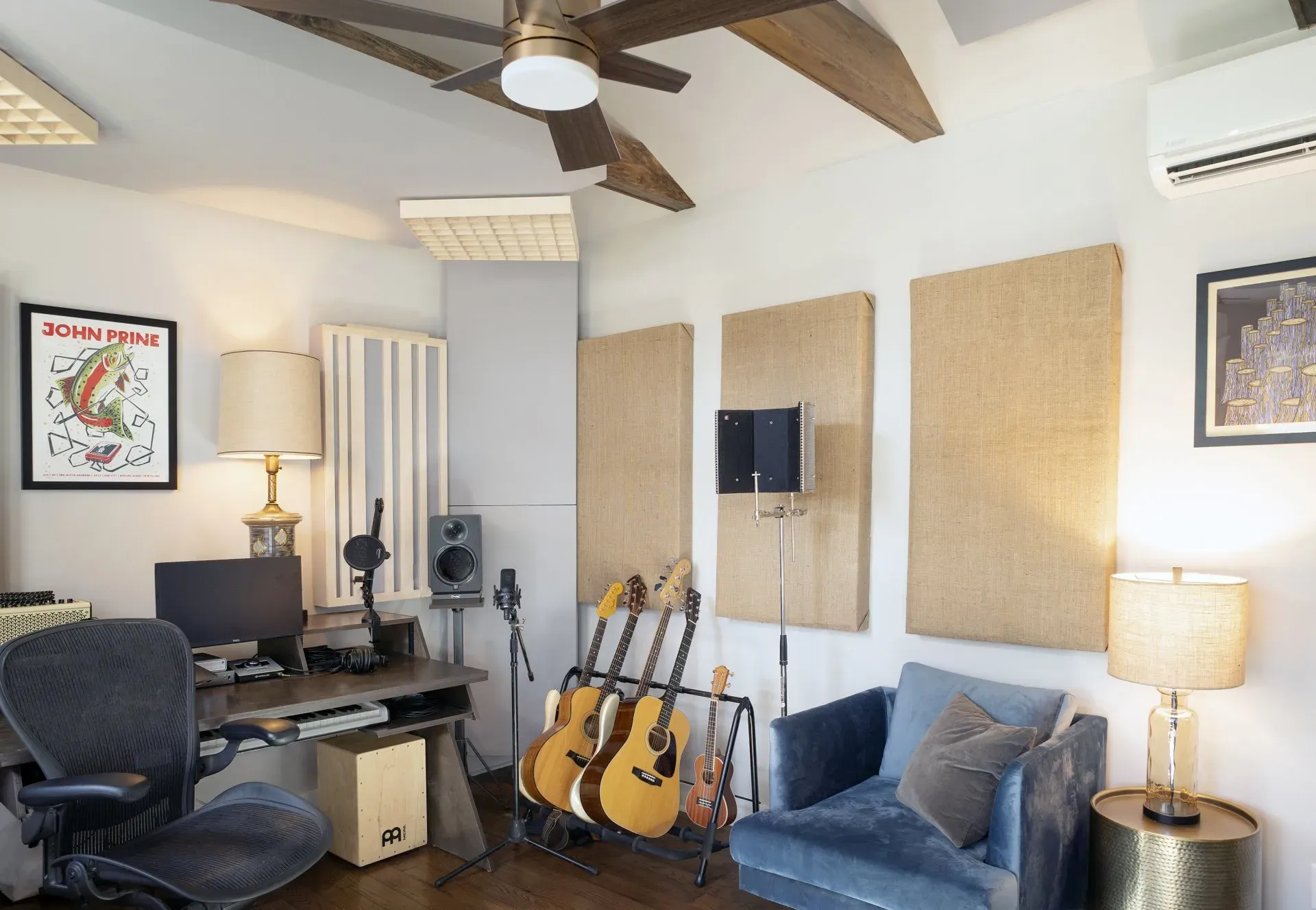 Home music studio with guitars, desk, blue chair, ceiling fan, lamps, and acoustic panels in a small room