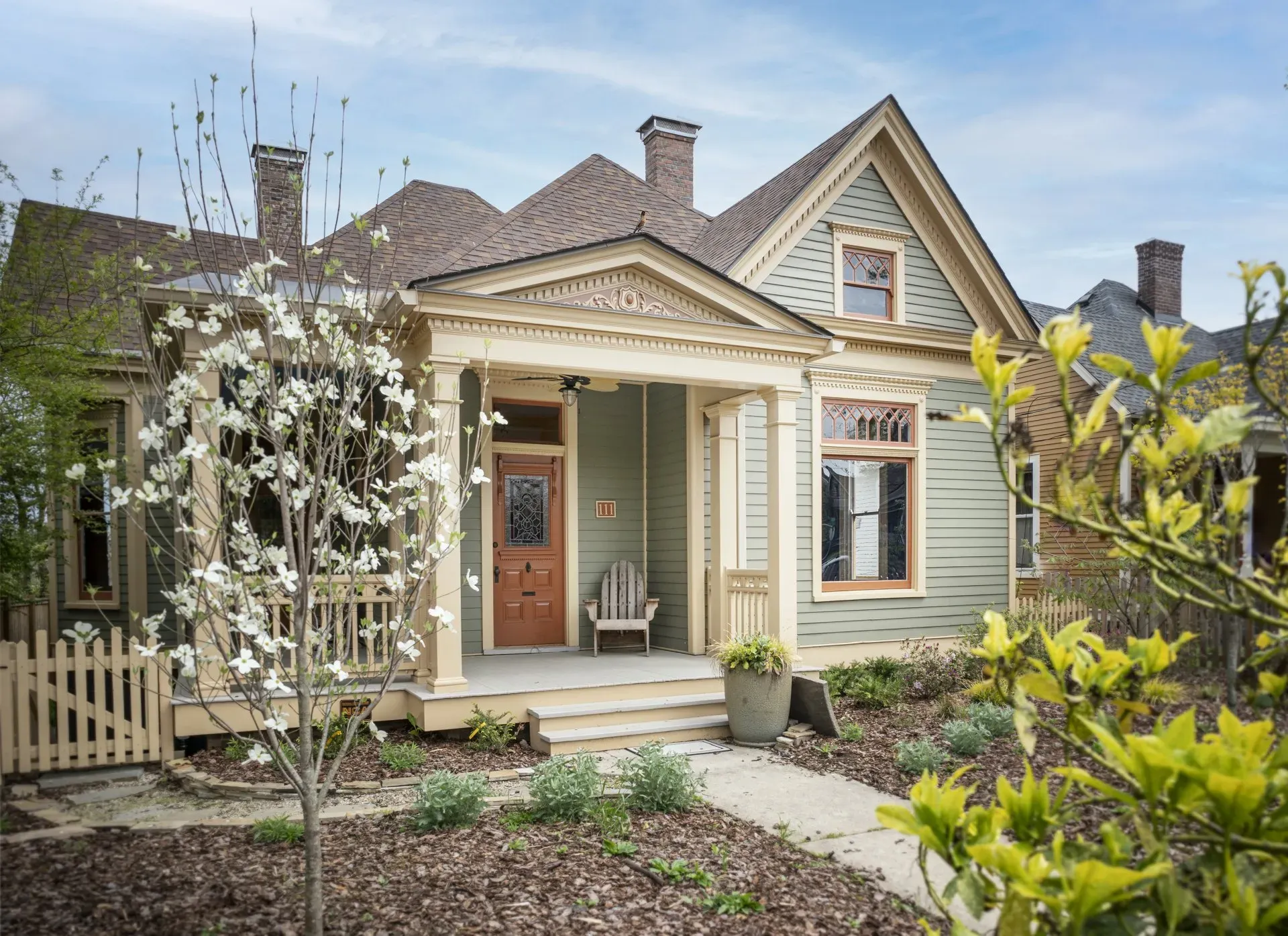 Front porch of a light blue house with white trim, potted plants, and a landscaped garden path