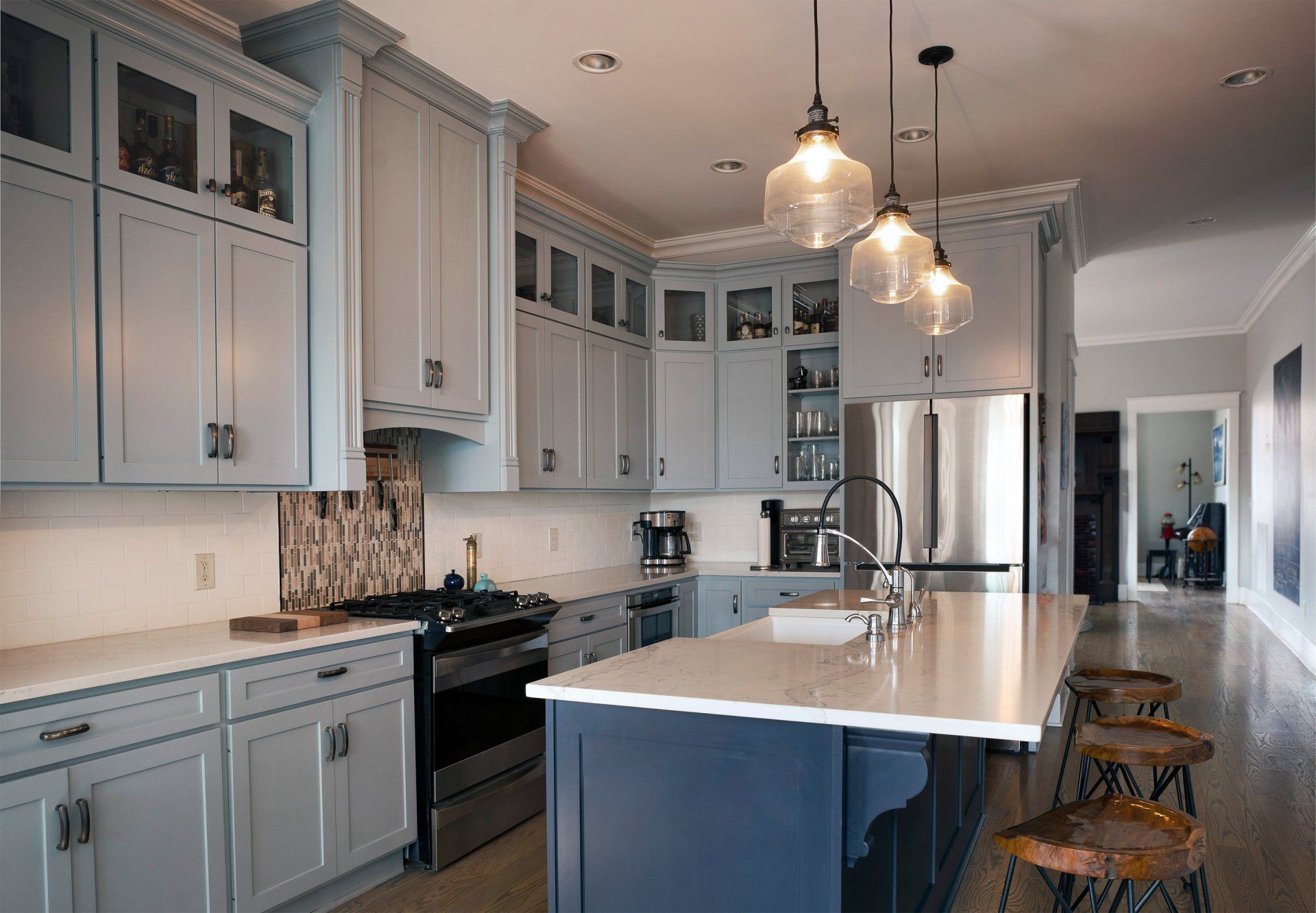 Modern kitchen with gray cabinets, white island, stainless fridge, and pendant lights