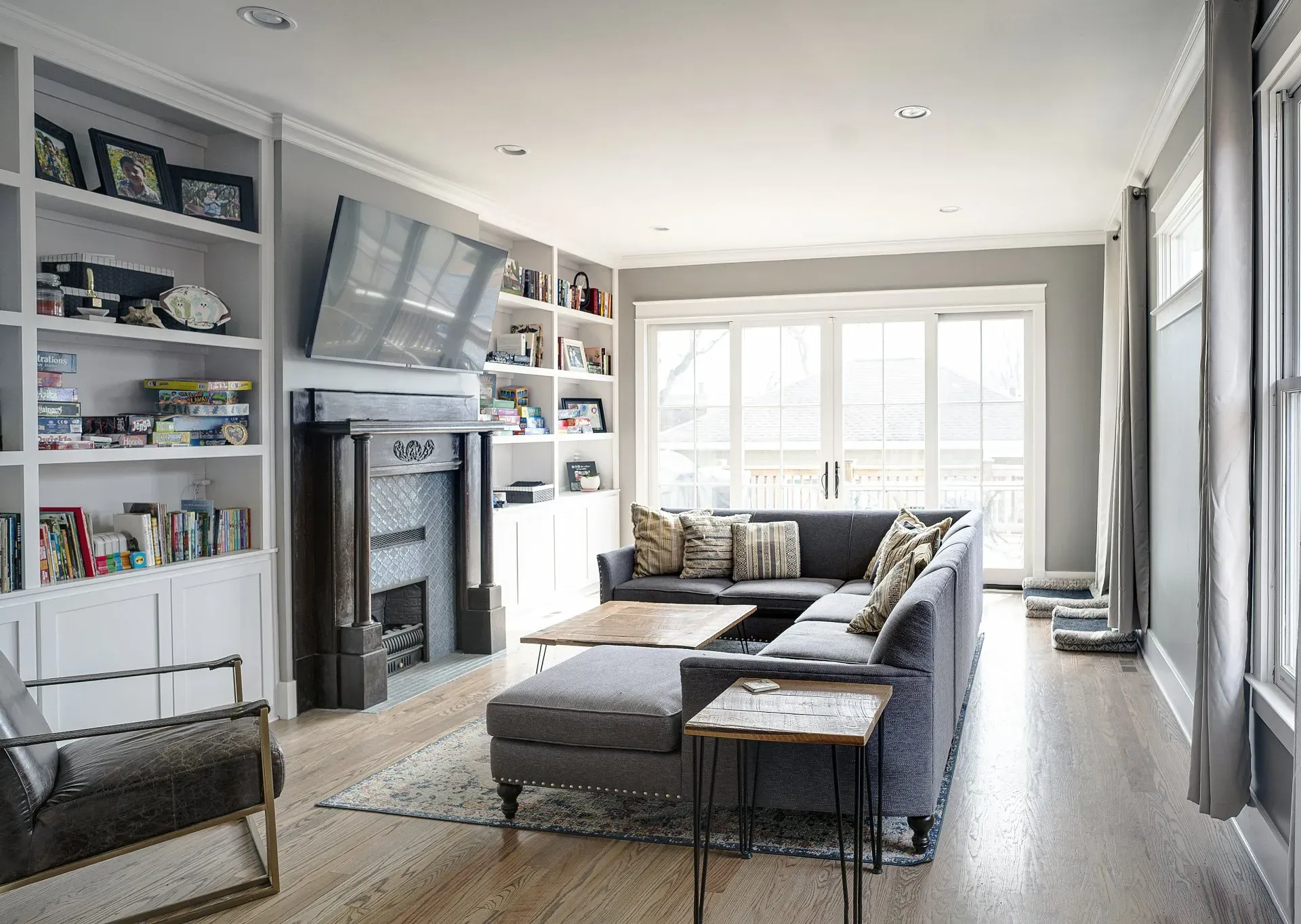Bright living room with gray sectional sofa, fireplace, built-in shelves, and large windows