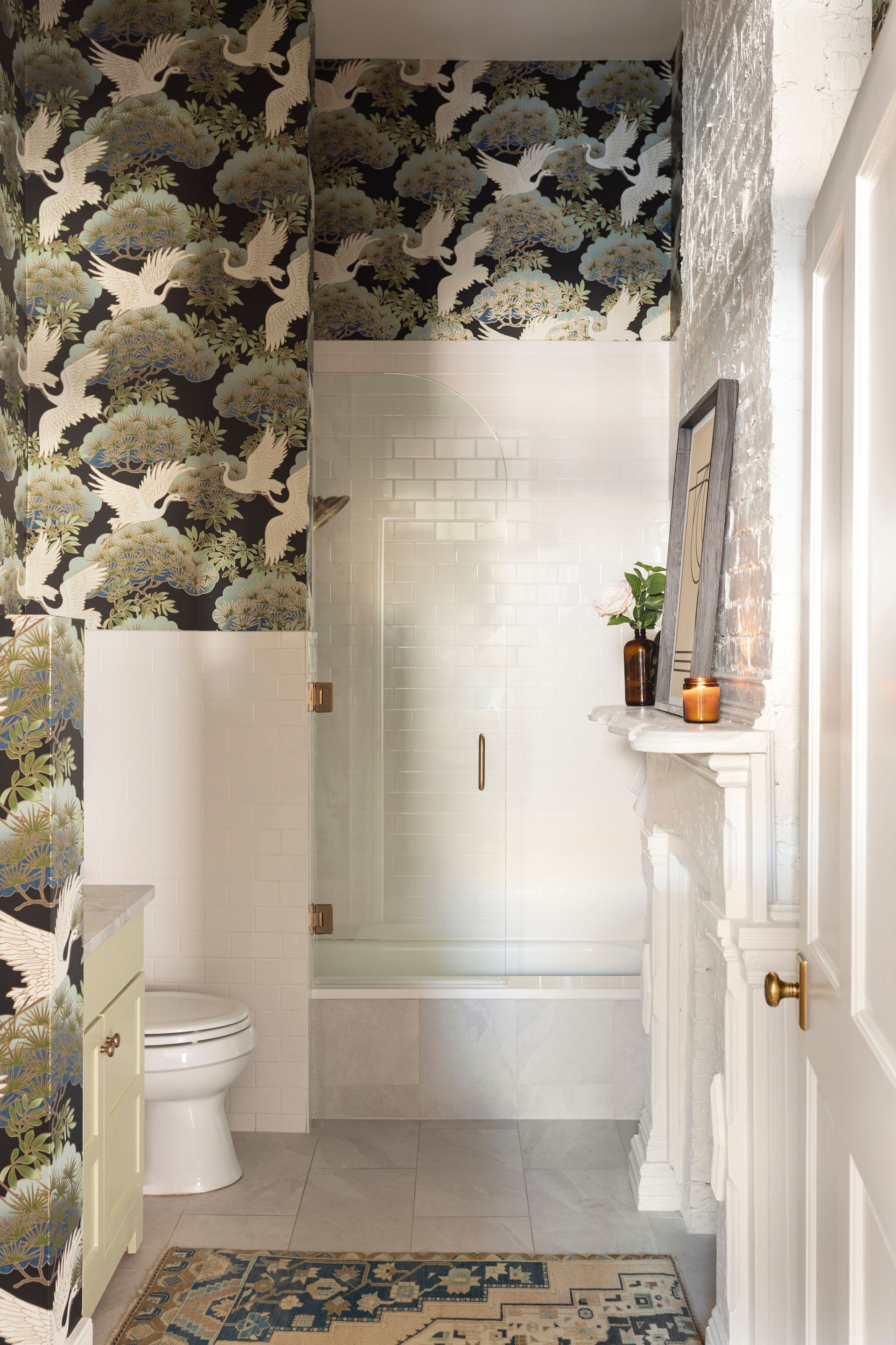 Floral wallpapered bathroom with white shower, toilet, vanity ledge, and tiled floor.