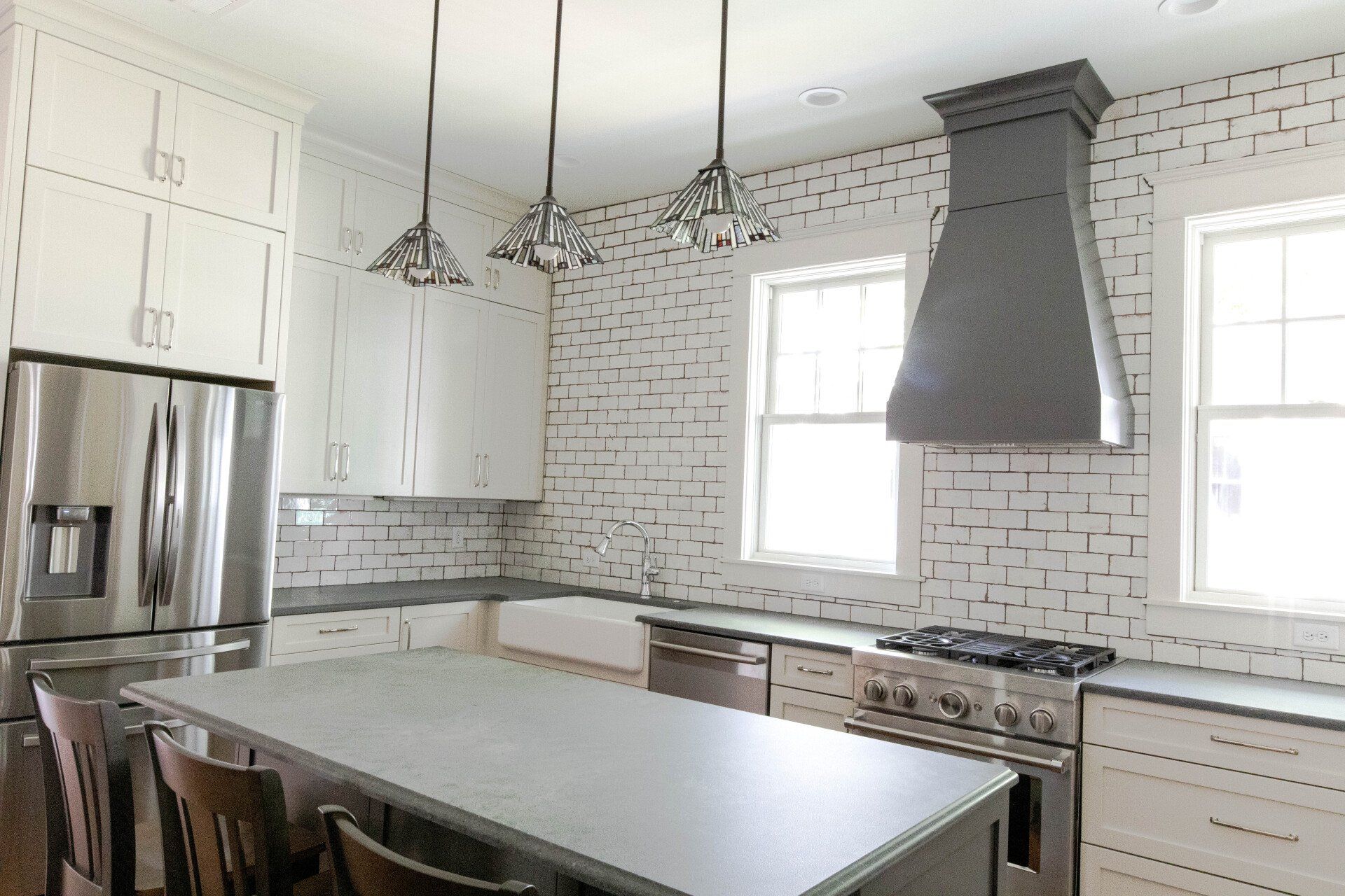 Modern white kitchen with stainless steel appliances, island, brick backsplash, and two windows