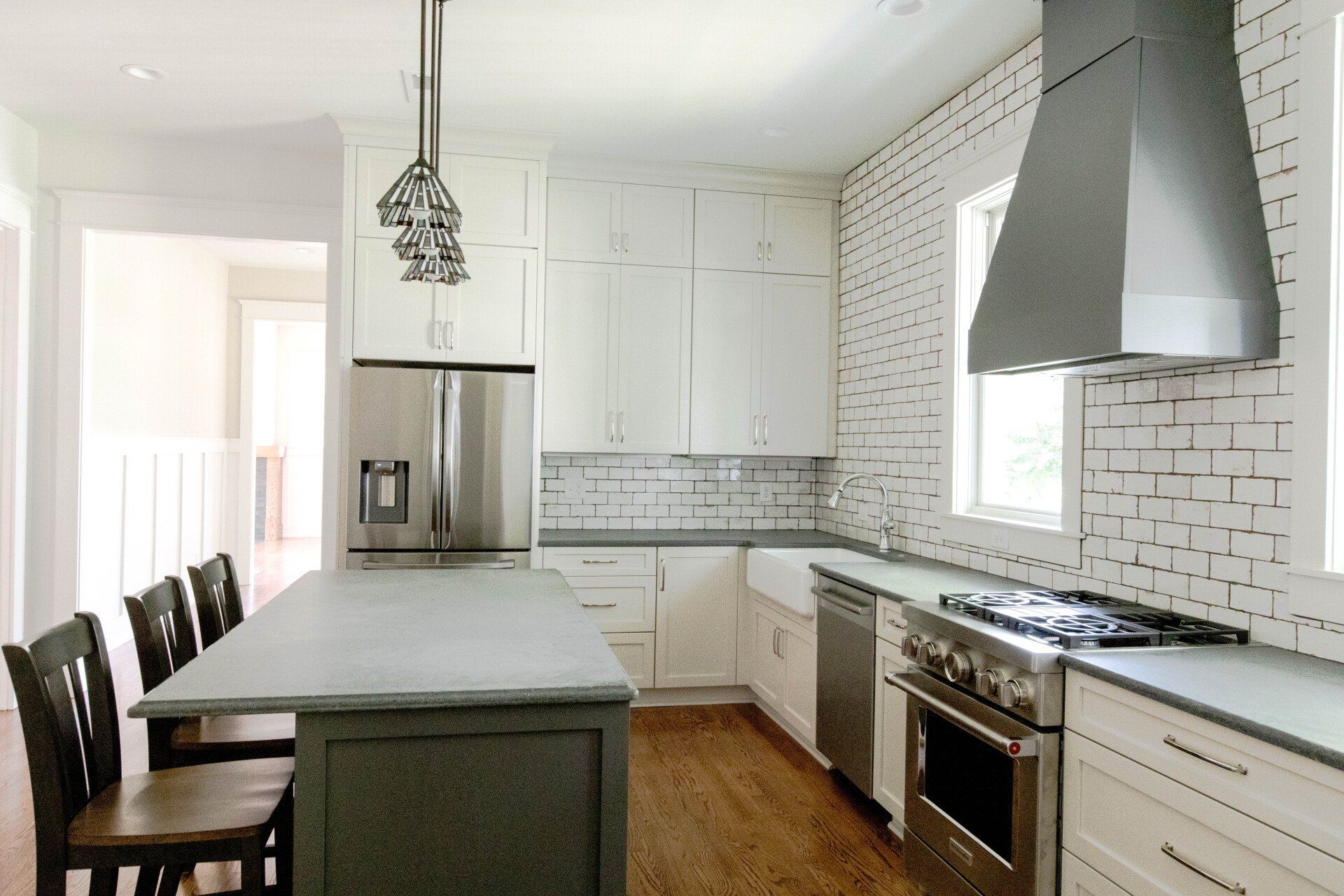 Modern white kitchen with island, stainless steel appliances, brick backsplash, and dark bar stools