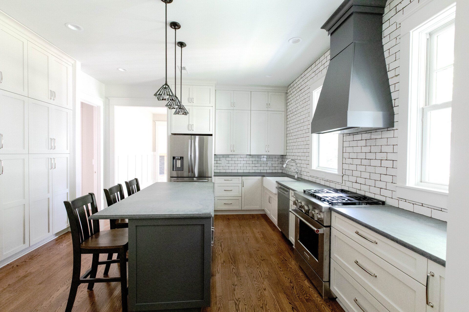 Bright white kitchen with island, stainless appliances, wood floor, and bar stools