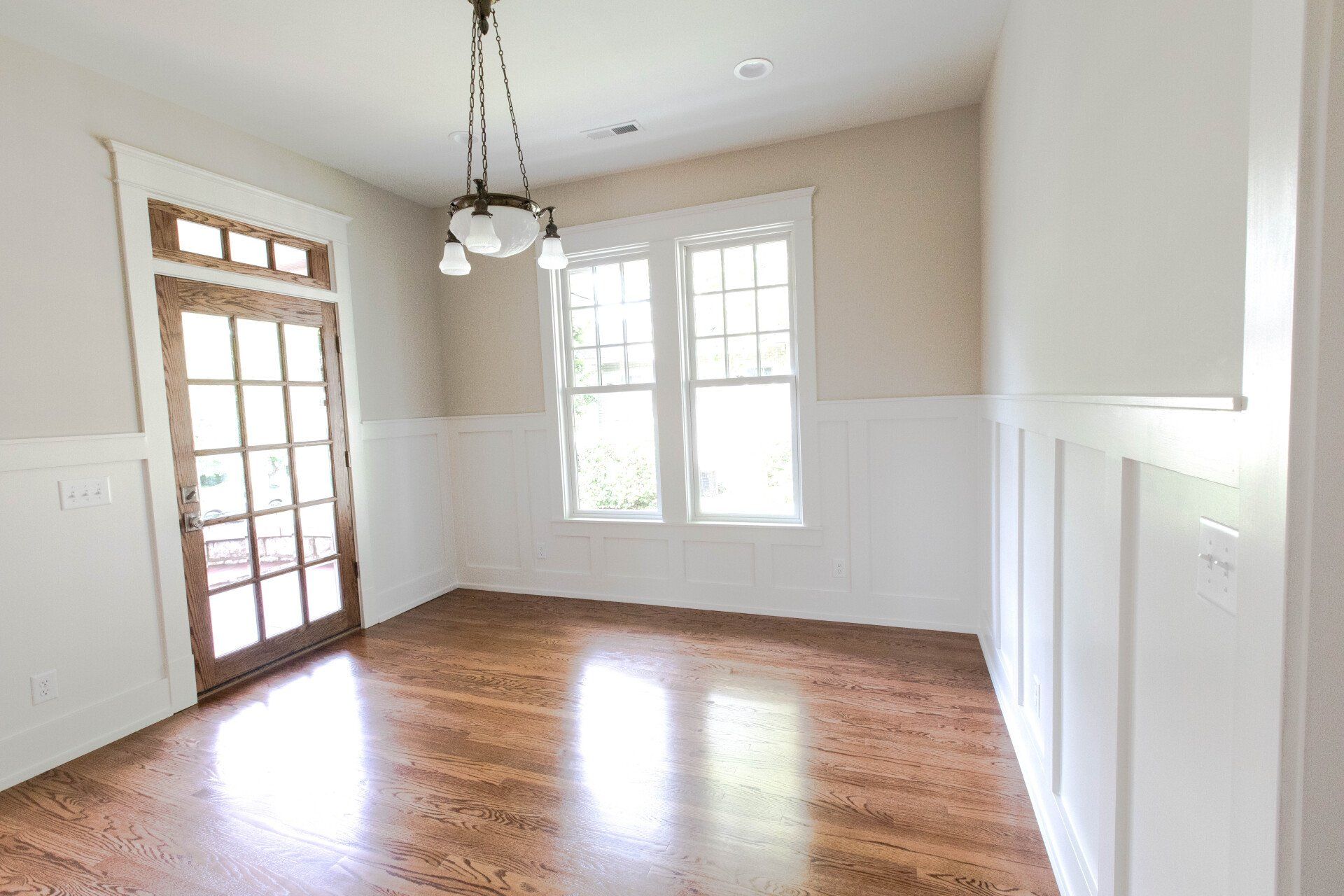 Empty dining room with hardwood floors, white wainscoting, and French doors leading outside.