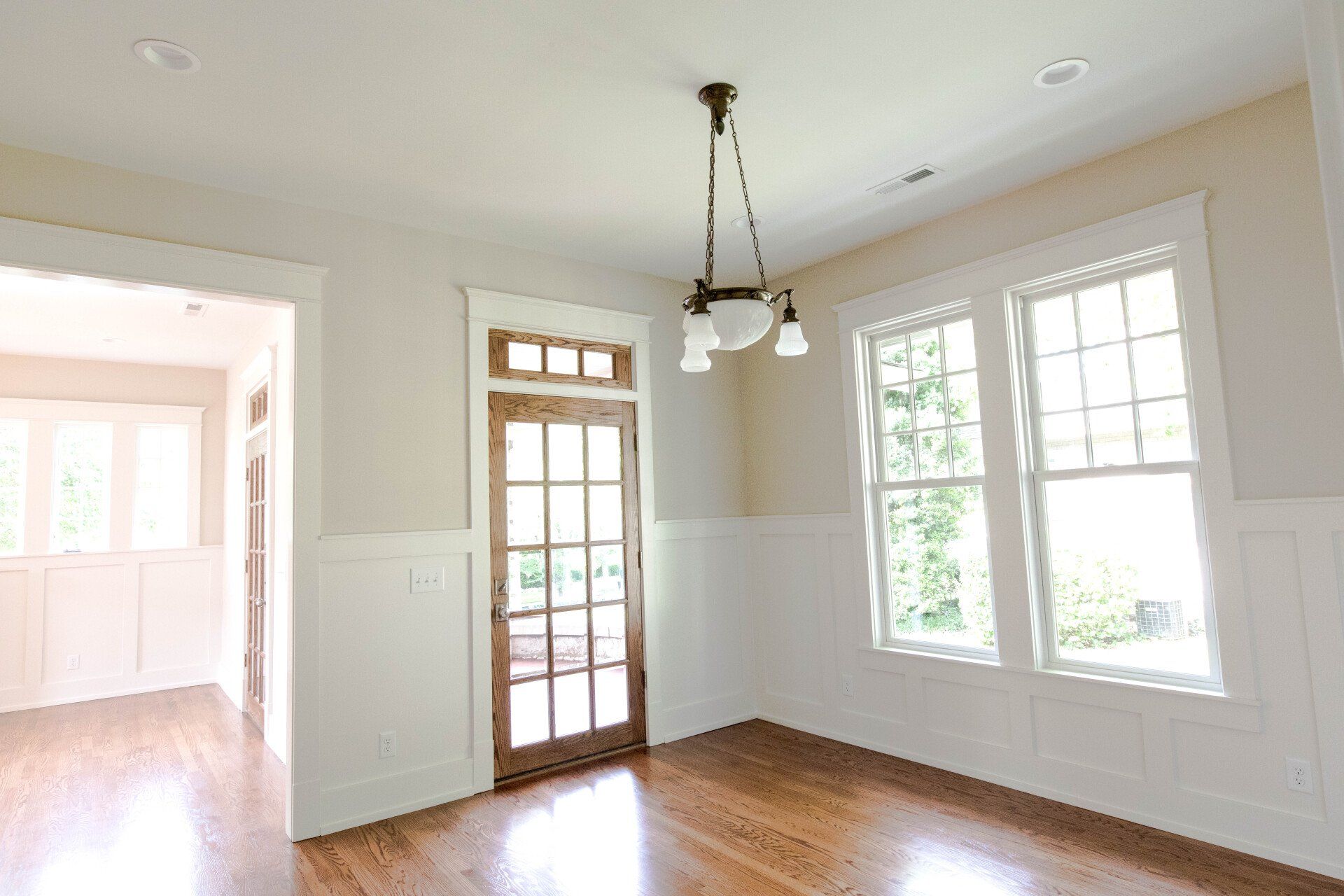 Empty bright dining room with hardwood floors, white walls, windows, and a glass-paned door