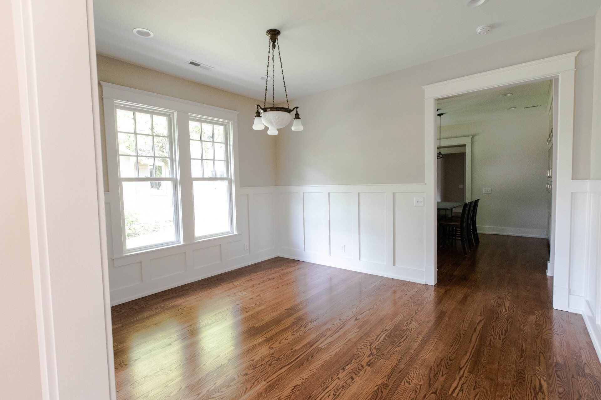Empty dining room with hardwood floors, white wainscoting, and large windows.