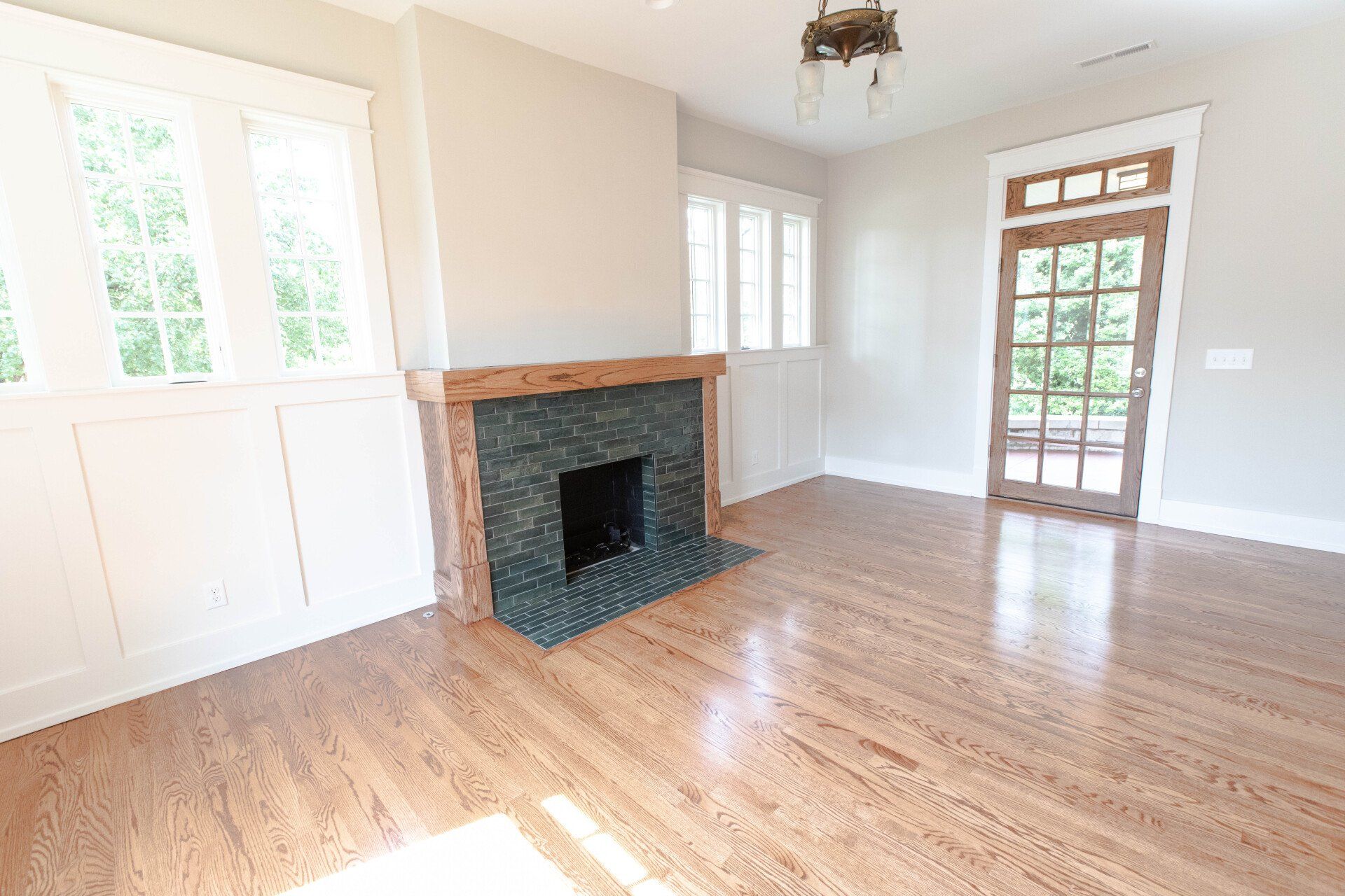 Empty living room with hardwood floors, white walls, a brick fireplace, and a glass-paneled door.
