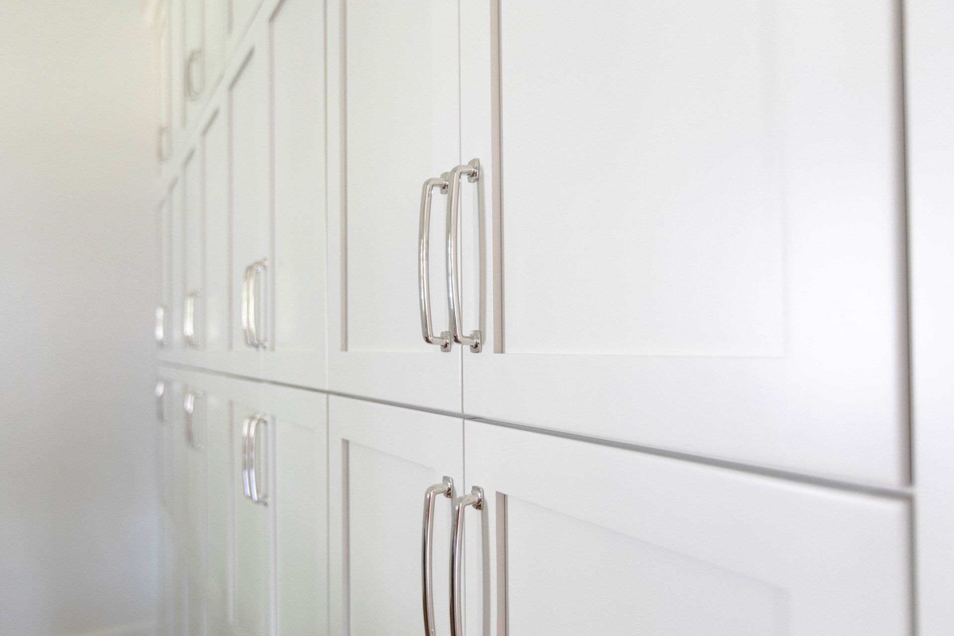 White built-in cabinet doors with silver handles along a bright wall