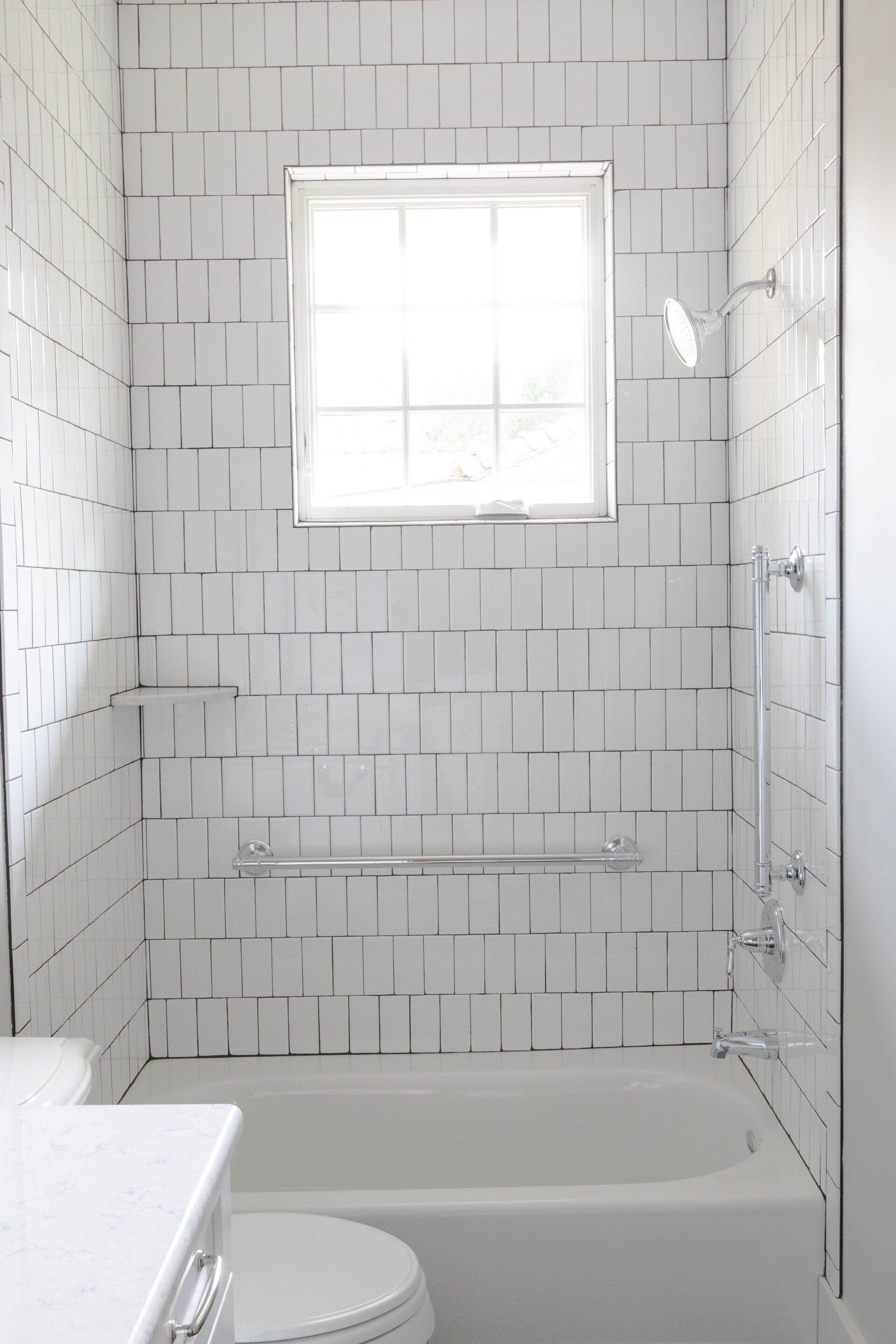 Small white-tiled bathroom with a bathtub, window, and towel rack under the window.