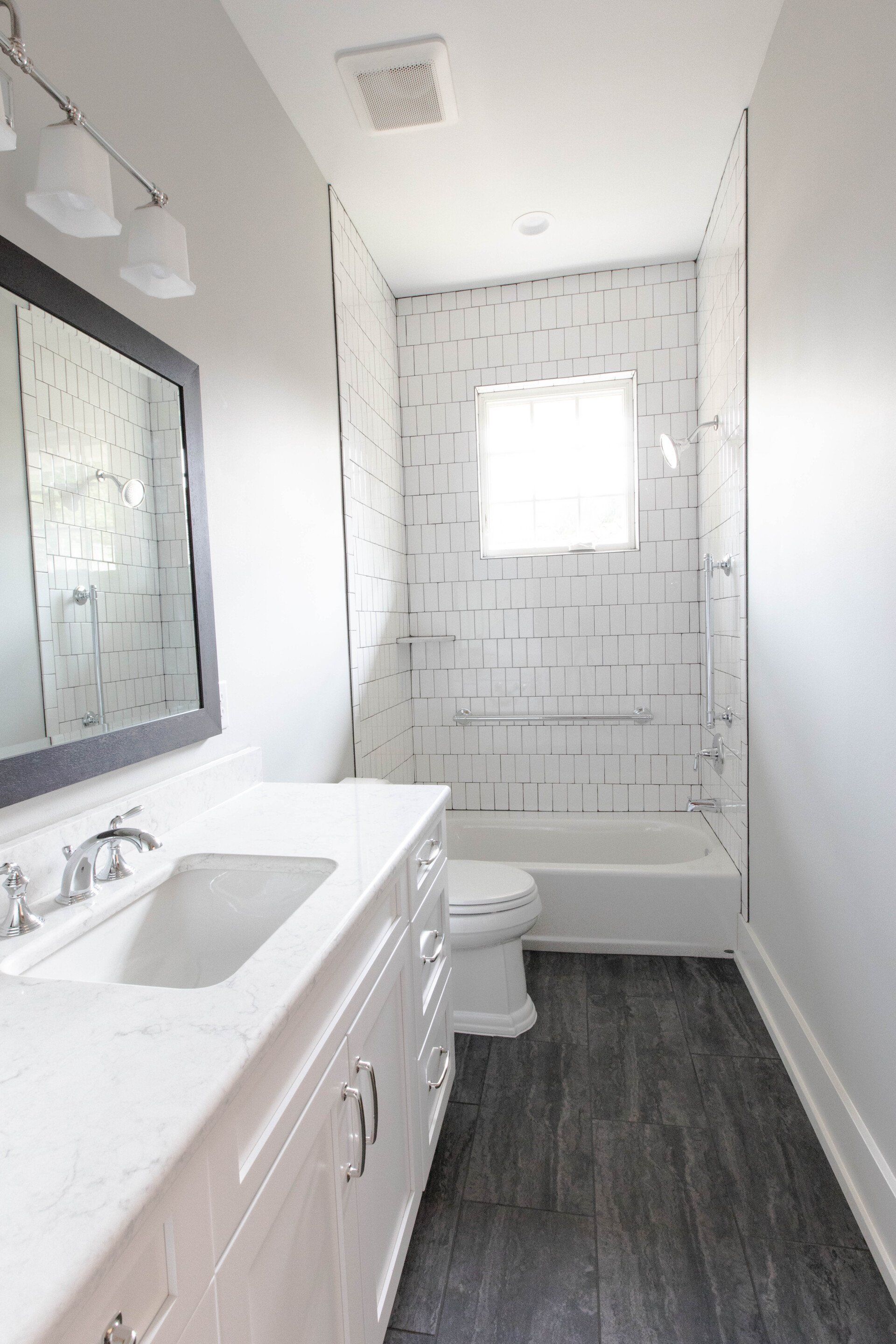 Narrow white bathroom with vanity, mirror, toilet, bathtub, and tiled shower wall