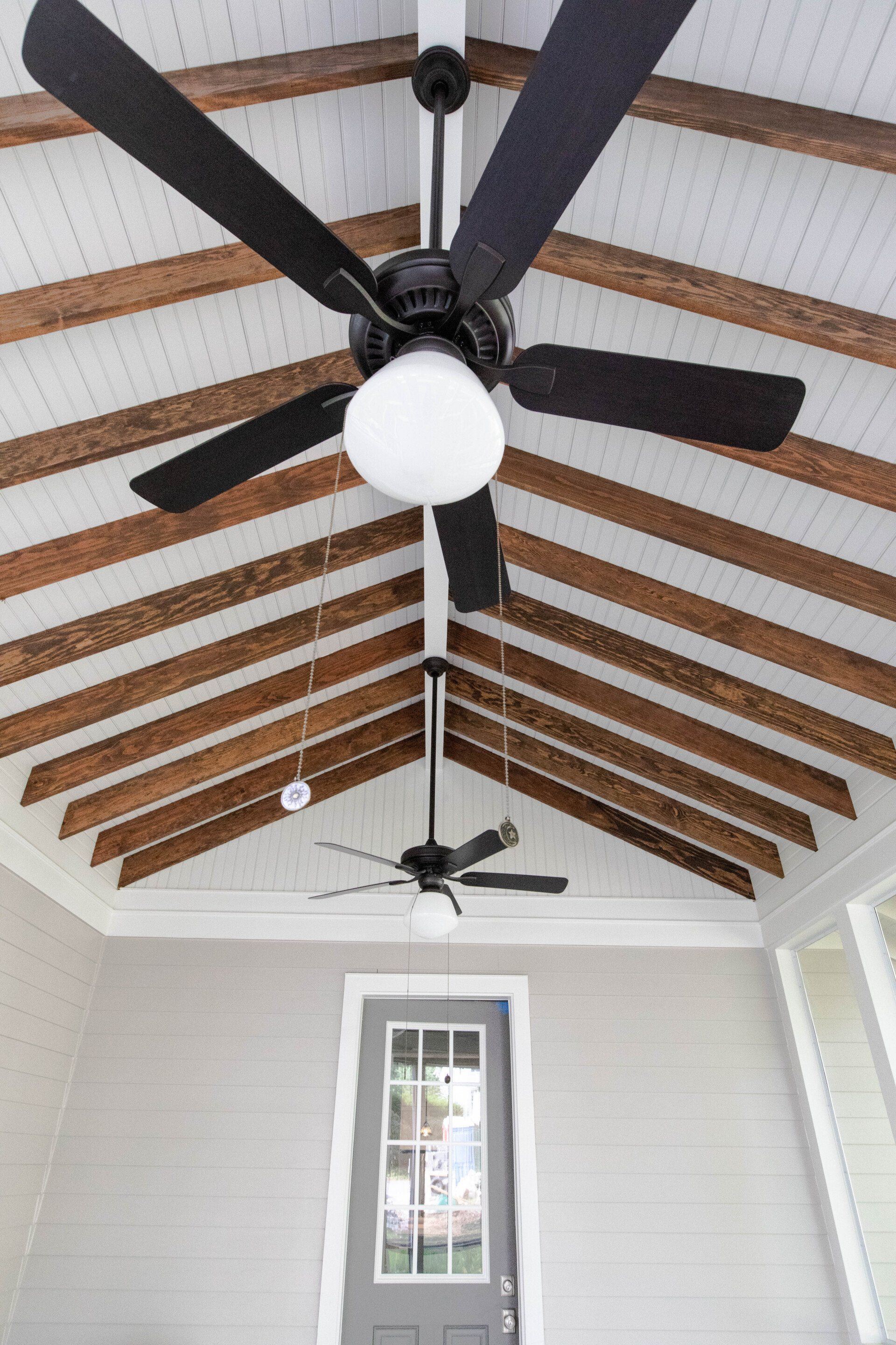 White vaulted porch ceiling with exposed beams and black ceiling fans above a door and windows.