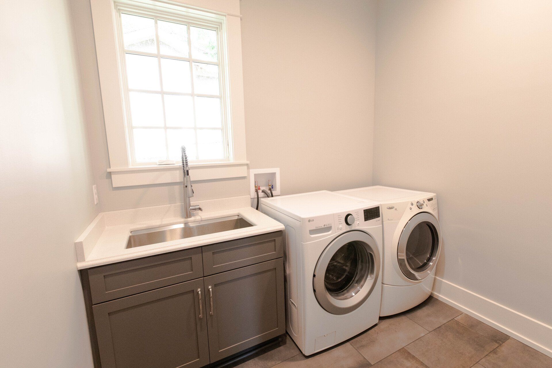 Laundry room with sink, window, and side-by-side washer and dryer on tile floor.