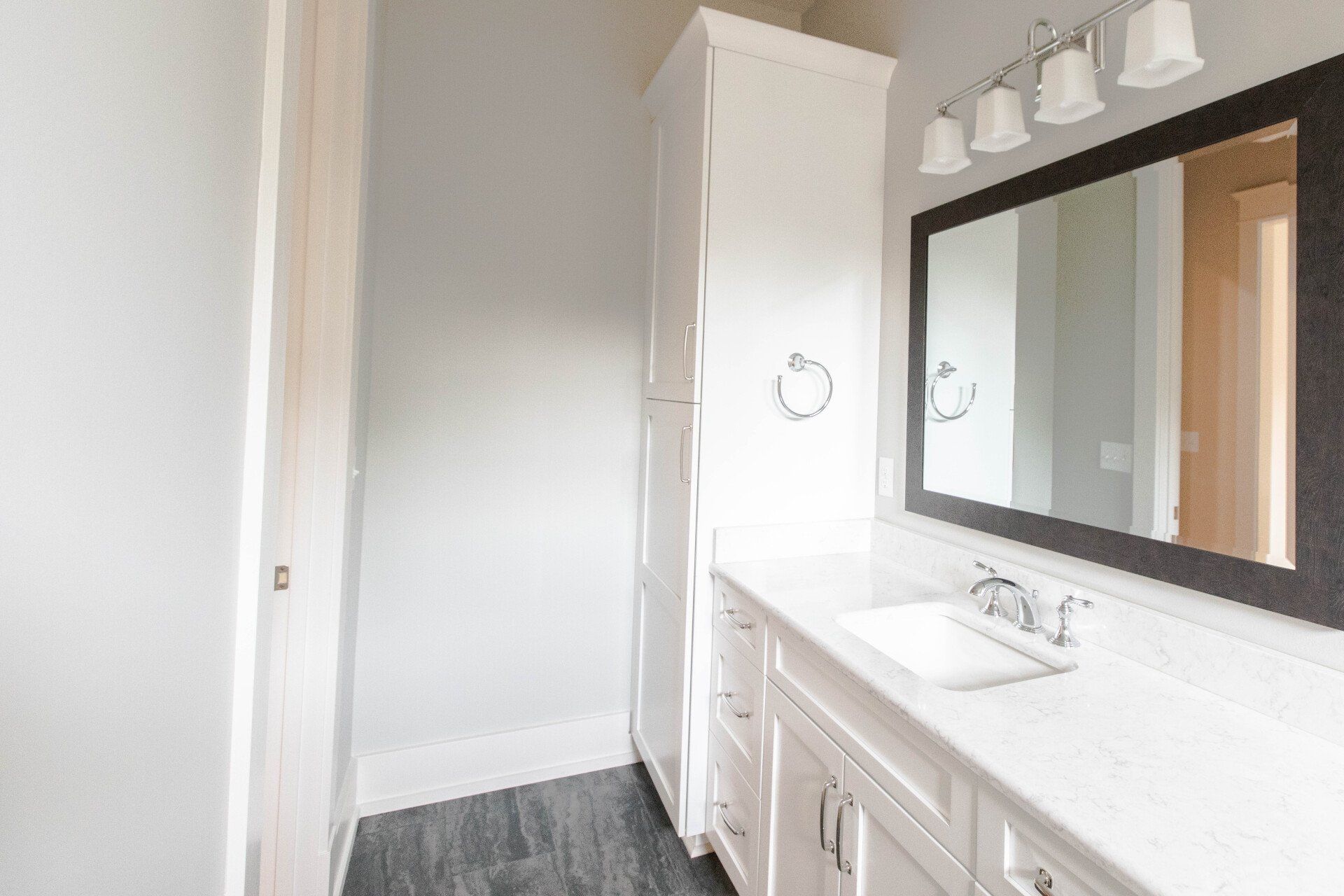 Bright bathroom vanity with mirror, sink, and white cabinets beside a doorway.