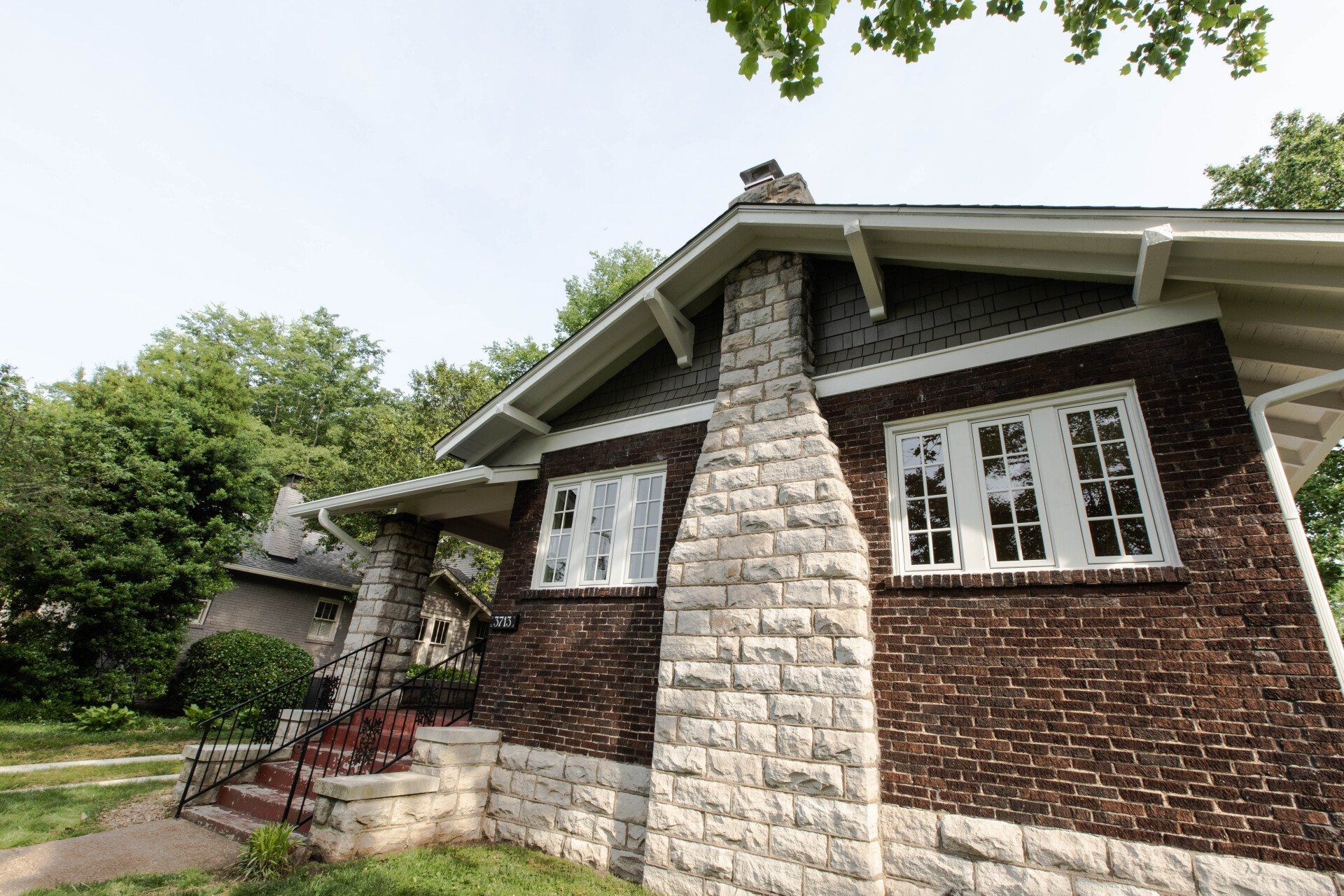 Brick house with stone chimney and front steps, surrounded by trees and greenery