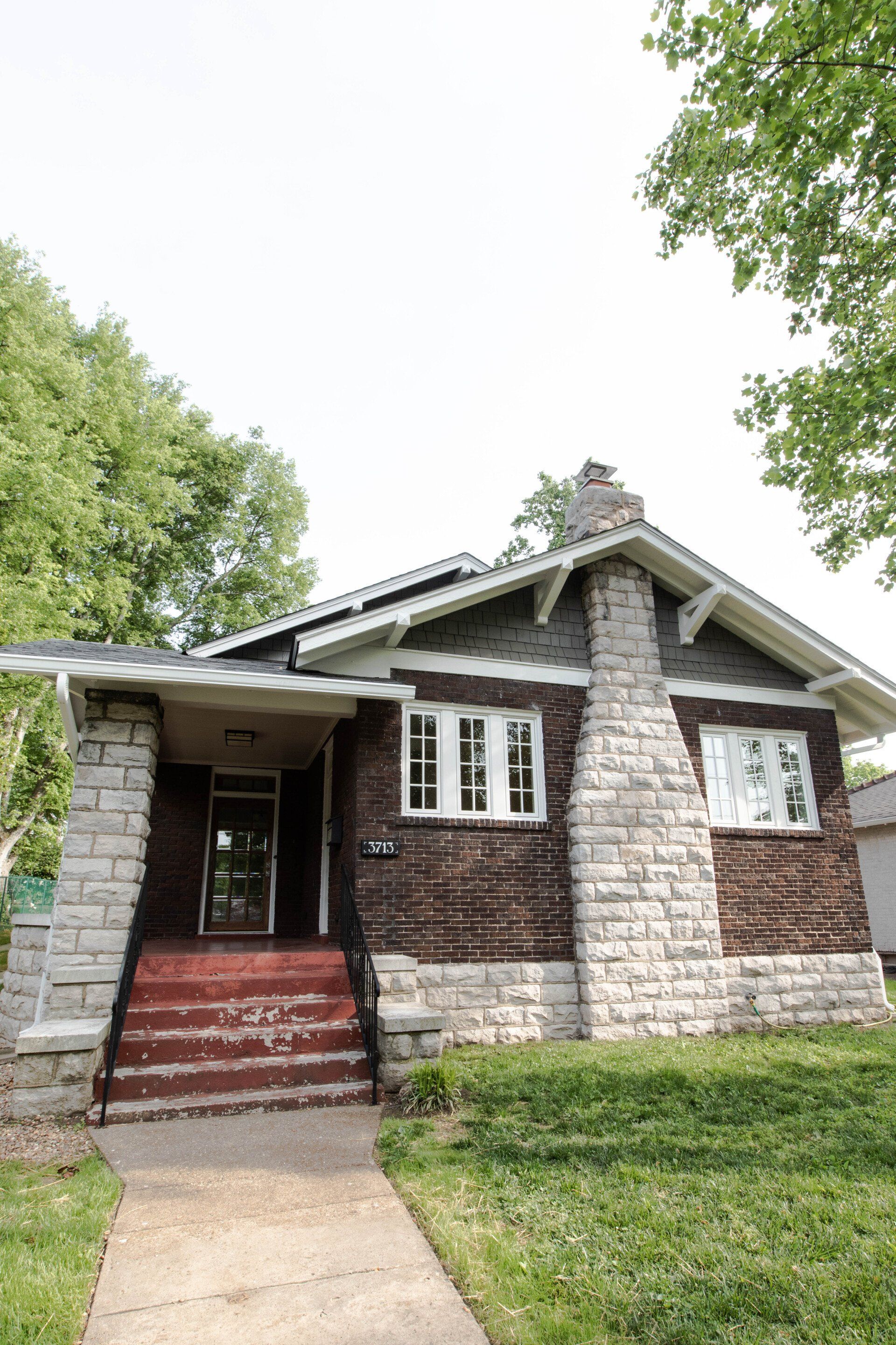 Brick bungalow with front steps, white stone trim, and a tree-lined yard