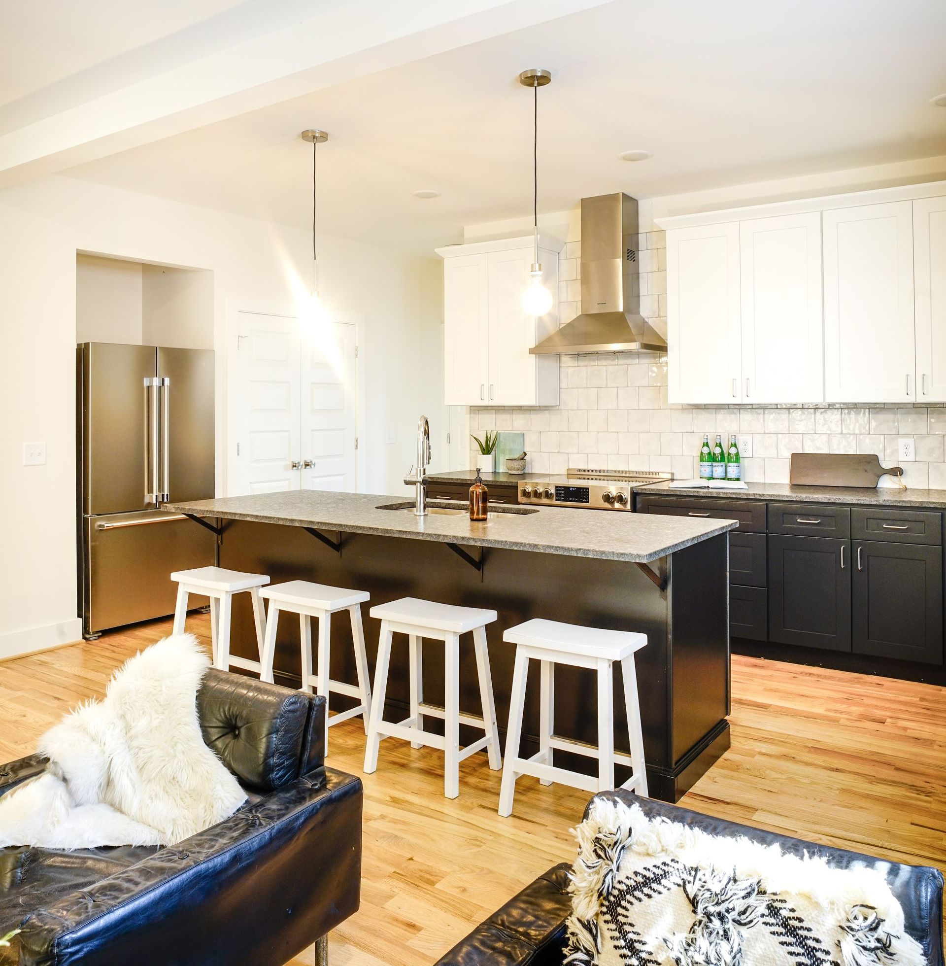Bright modern kitchen with white cabinets, black island, bar stools, and stainless steel appliances