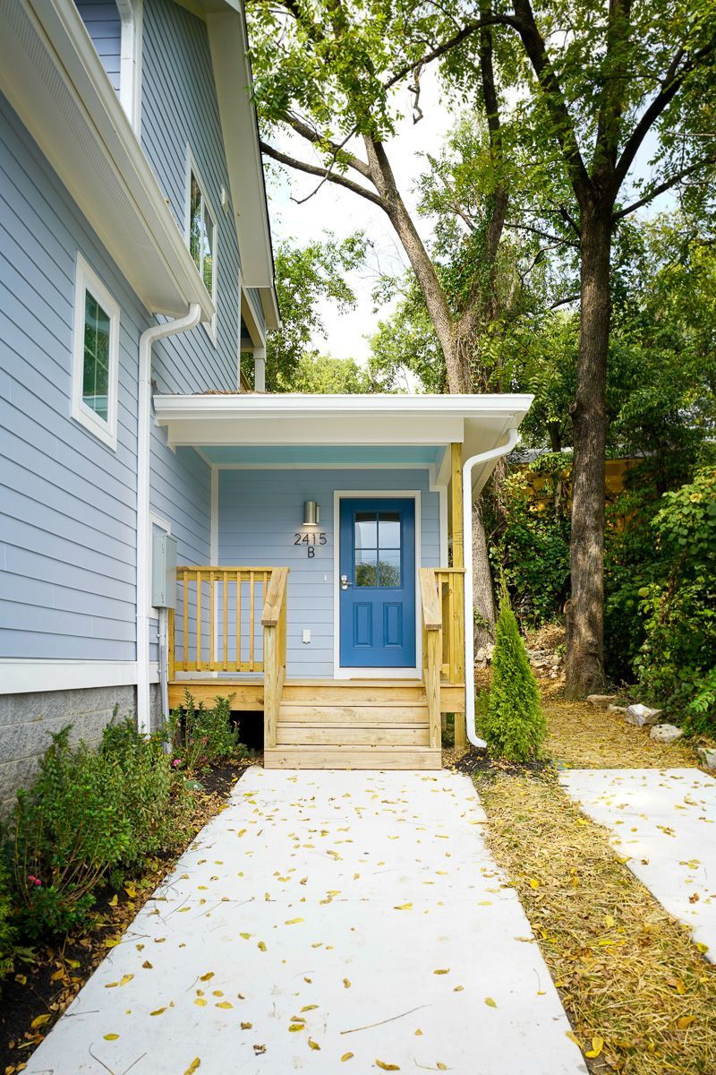 Front walkway to a blue house with a small porch and steps, lined by trees and grass